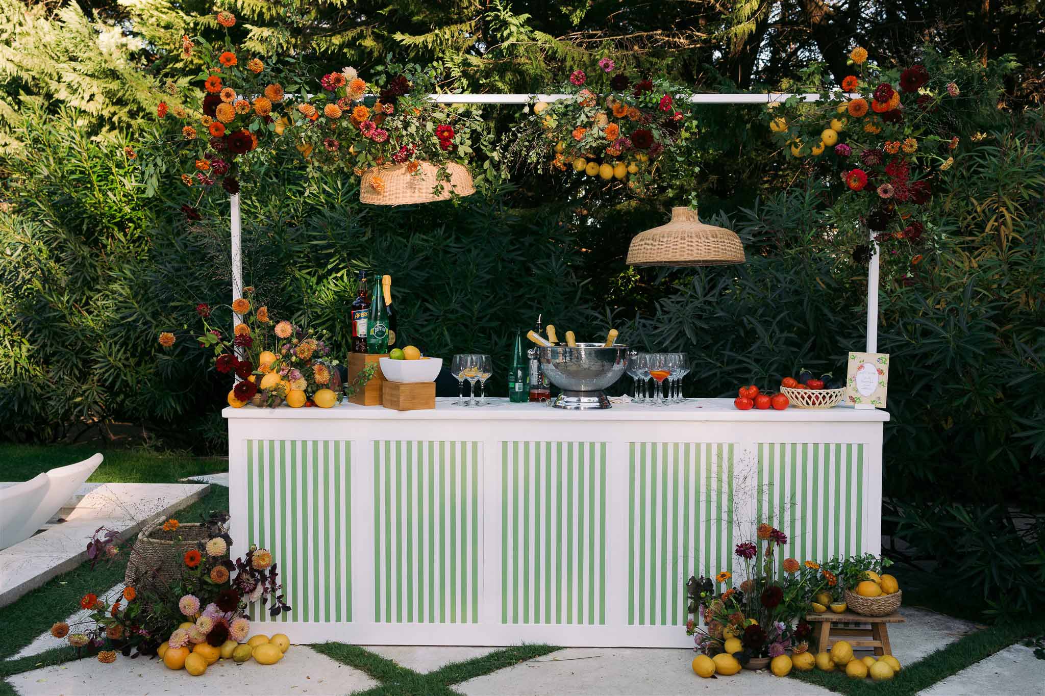 Outdoor wedding bar with floral installation and sage green striping in garden setting