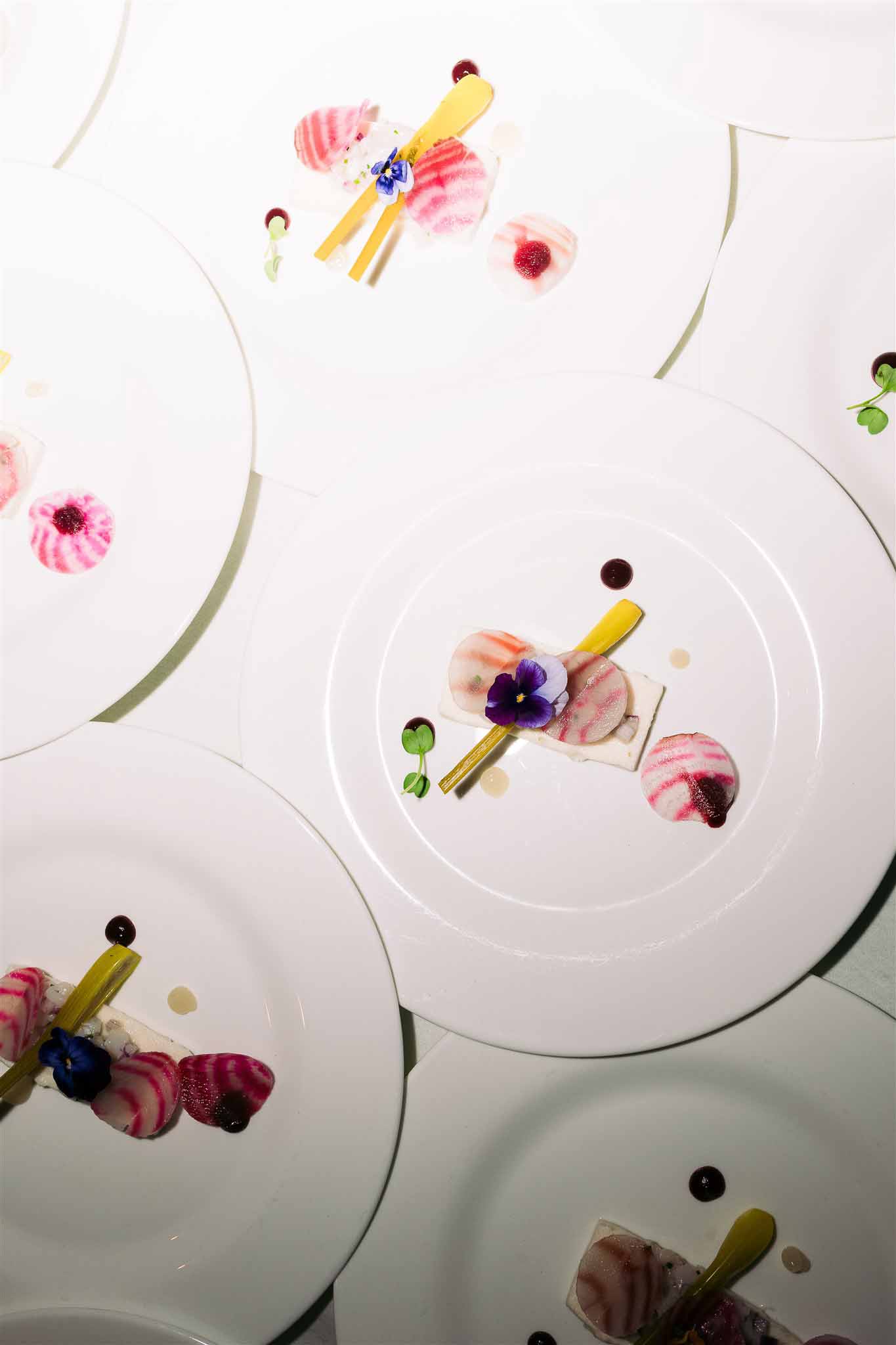 Overhead flat lay of wedding place settings with floral arrangements and gold utensils on white plates