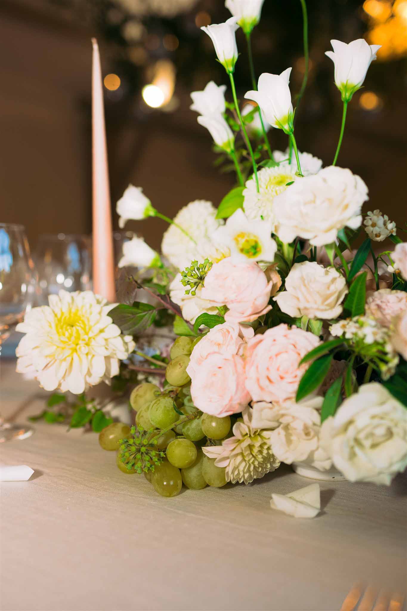 Wedding reception table centerpiece with ivory and pink flowers and rose gold candle at indoor venue
