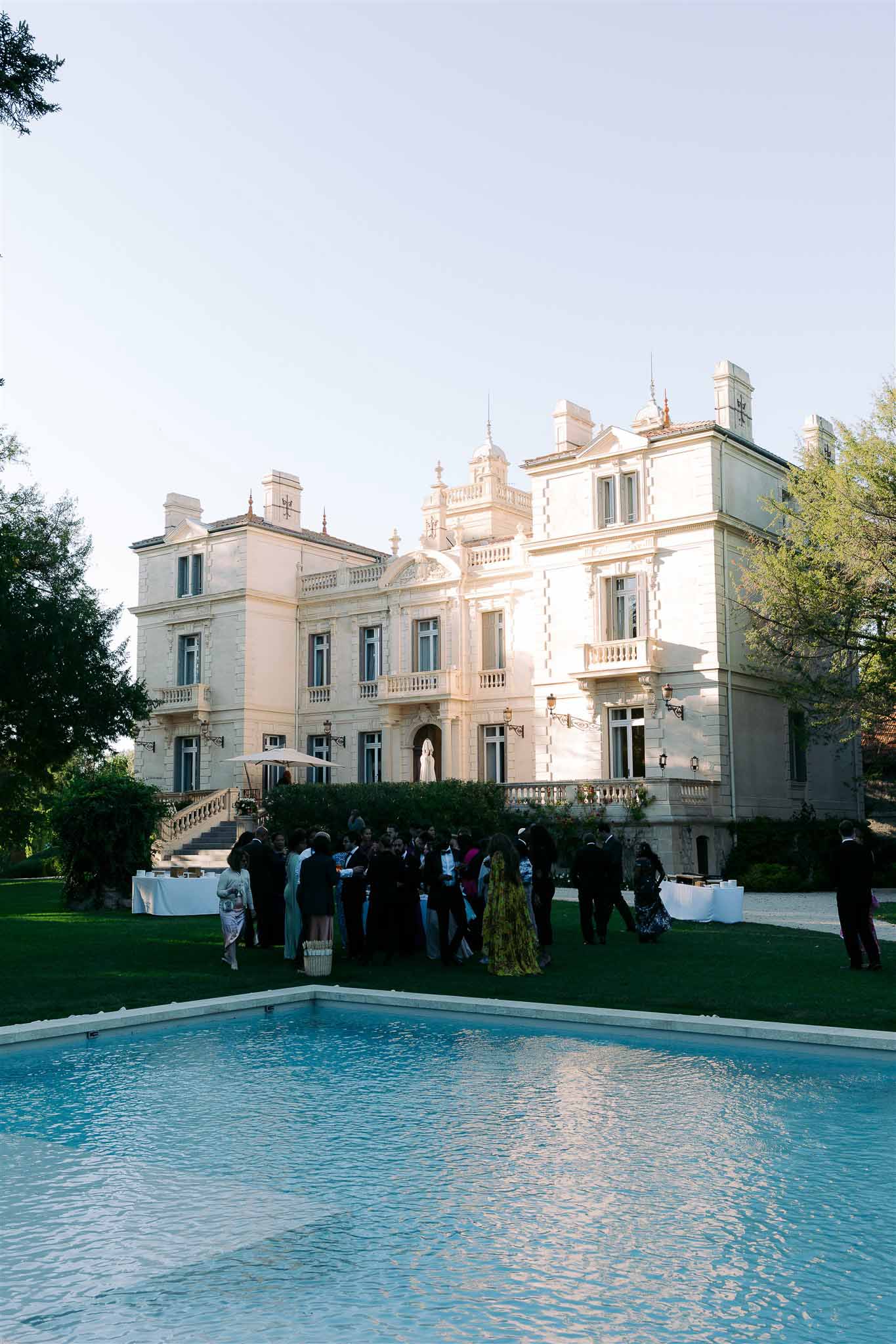 Cocktail hour reception on manicured lawn of neoclassical estate with guests and pool