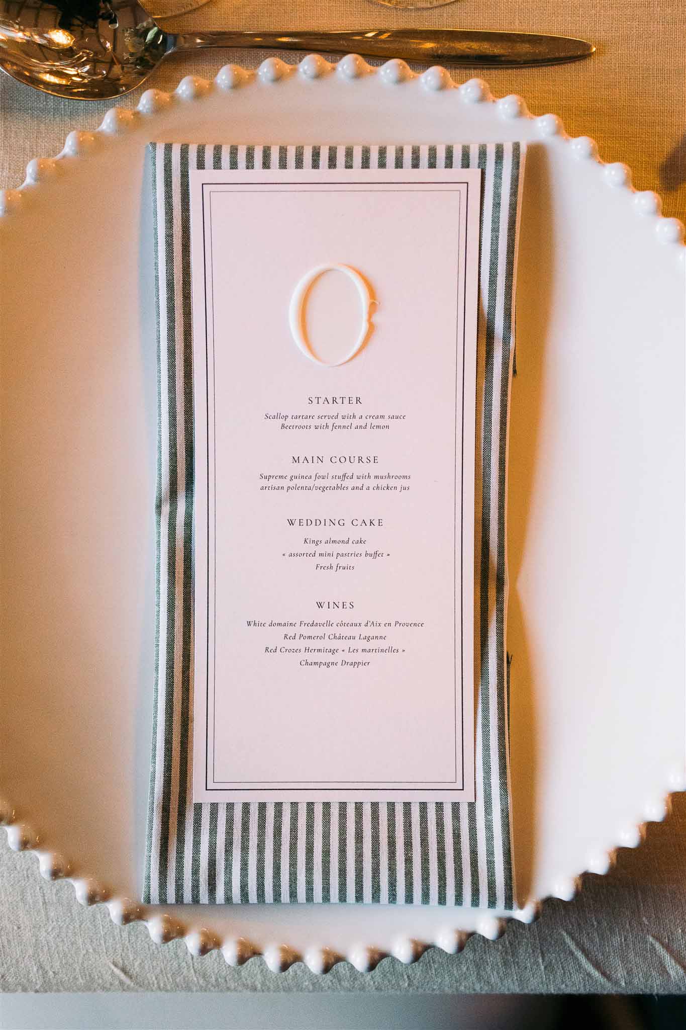 Wedding reception menu card on beaded white plate with striped napkin and gold utensils