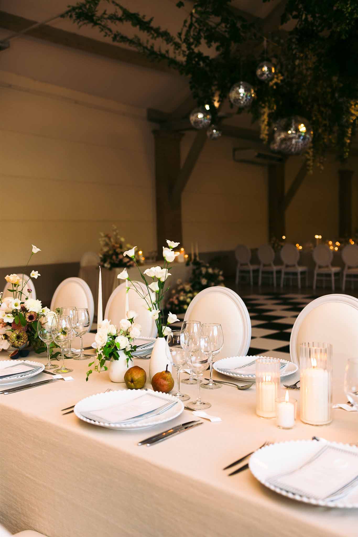 Reception table setting with white linens and candles in indoor ballroom with wooden beams