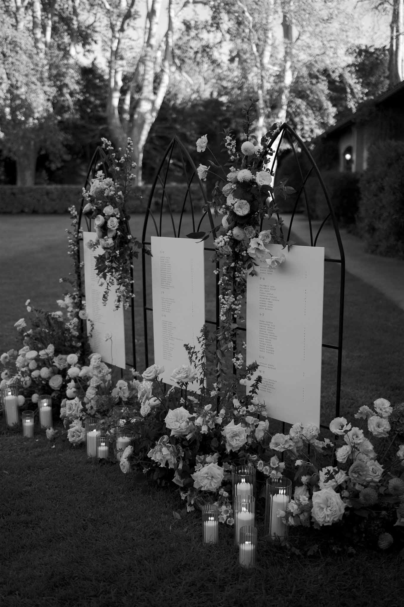 Black and white seating chart installation with floral arrangements and candles in outdoor garden setting