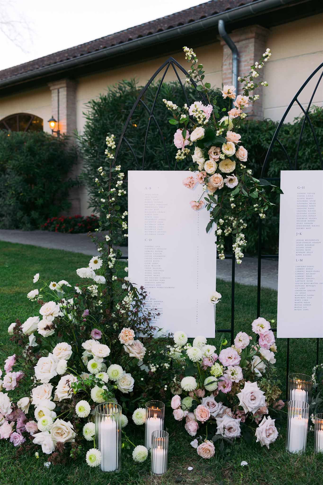 Seating chart display with floral arches and candles at European villa courtyard wedding