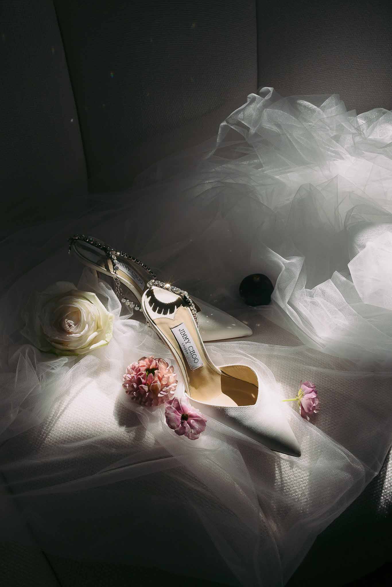 Bridal accessories flat lay with ivory heels, sunglasses, and flowers on tulle fabric