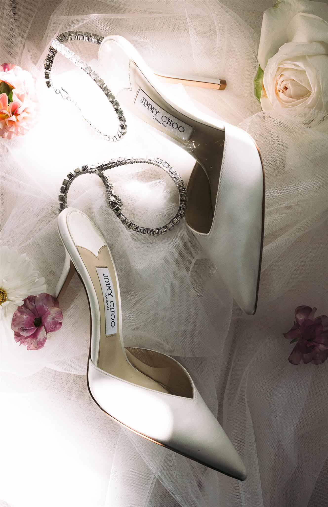 Bridal accessories flat lay with Jimmy Choo shoes, crystal bracelets, and flowers on ivory tulle