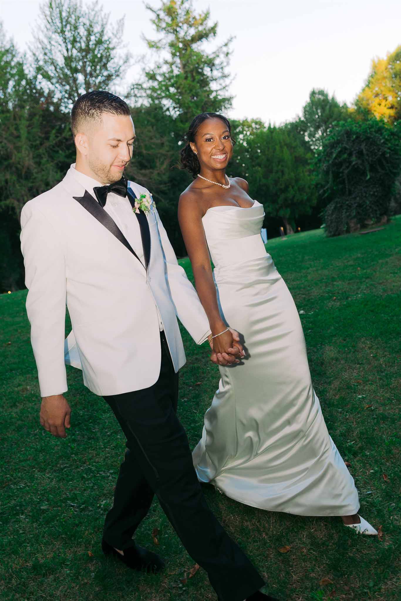 Newlywed couple walking hand in hand on garden lawn during reception