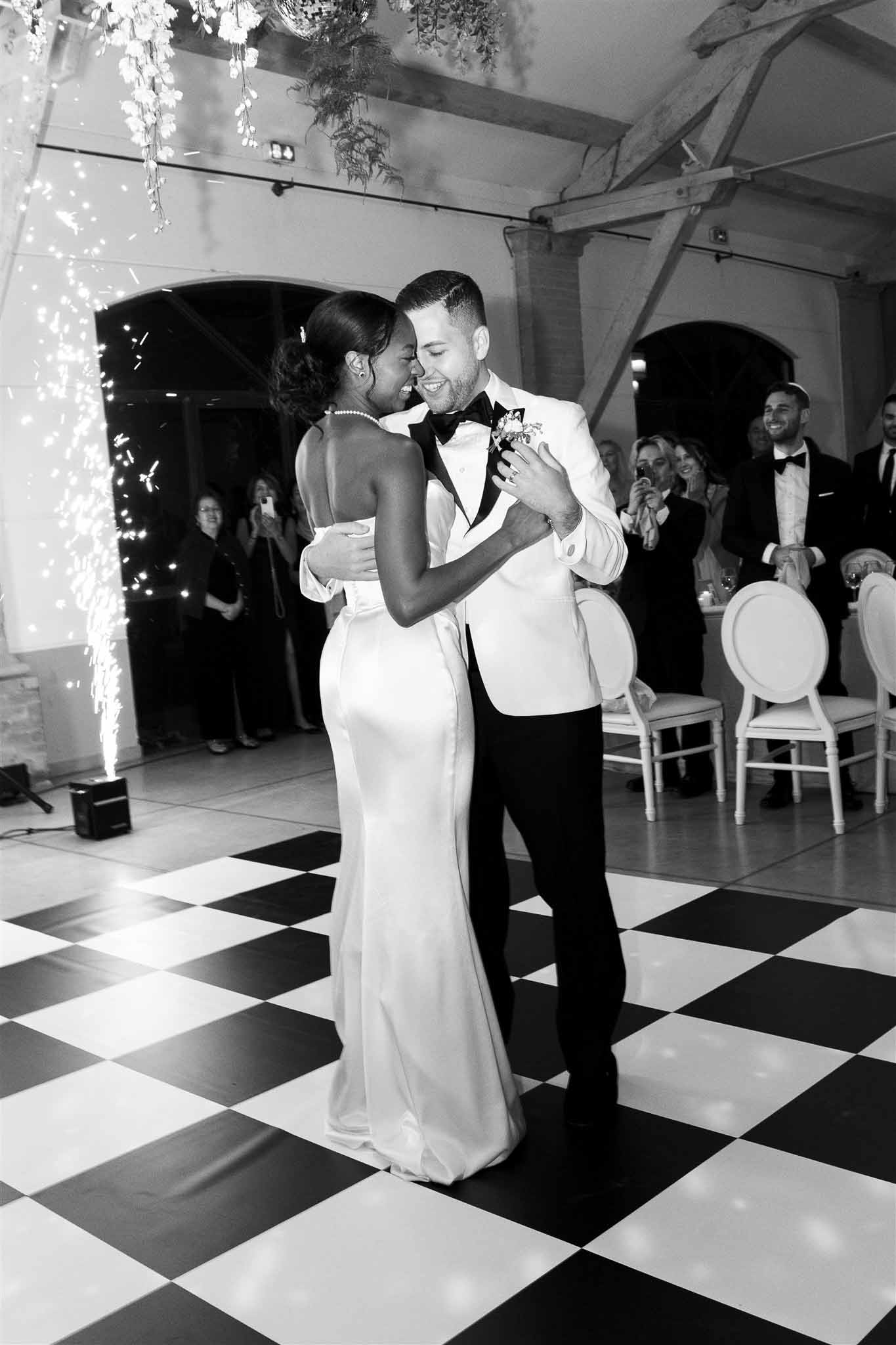 Couple's first dance on checkered floor in industrial venue with exposed beams and brick archways