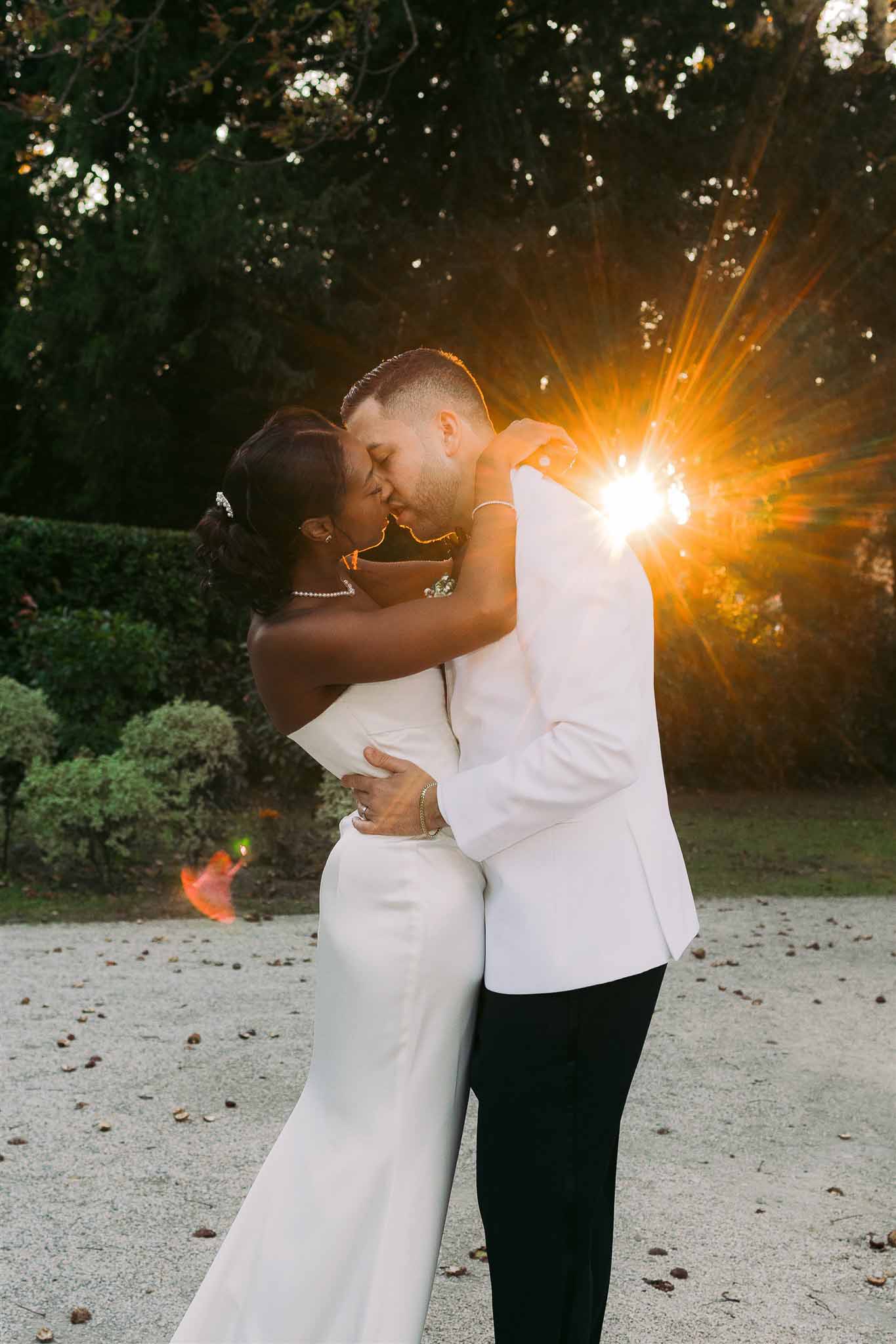 Bride and groom kissing during evening portrait session in garden courtyard with dramatic golden lighting