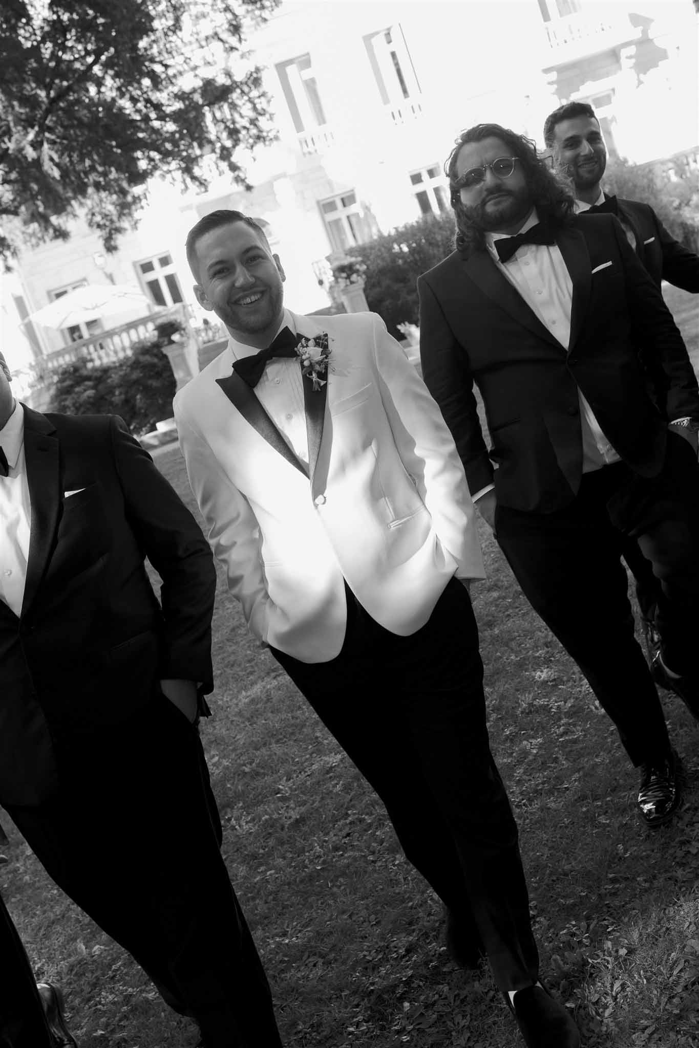 Groom and groomsmen in formal tuxedos posing outdoors against classical architecture backdrop