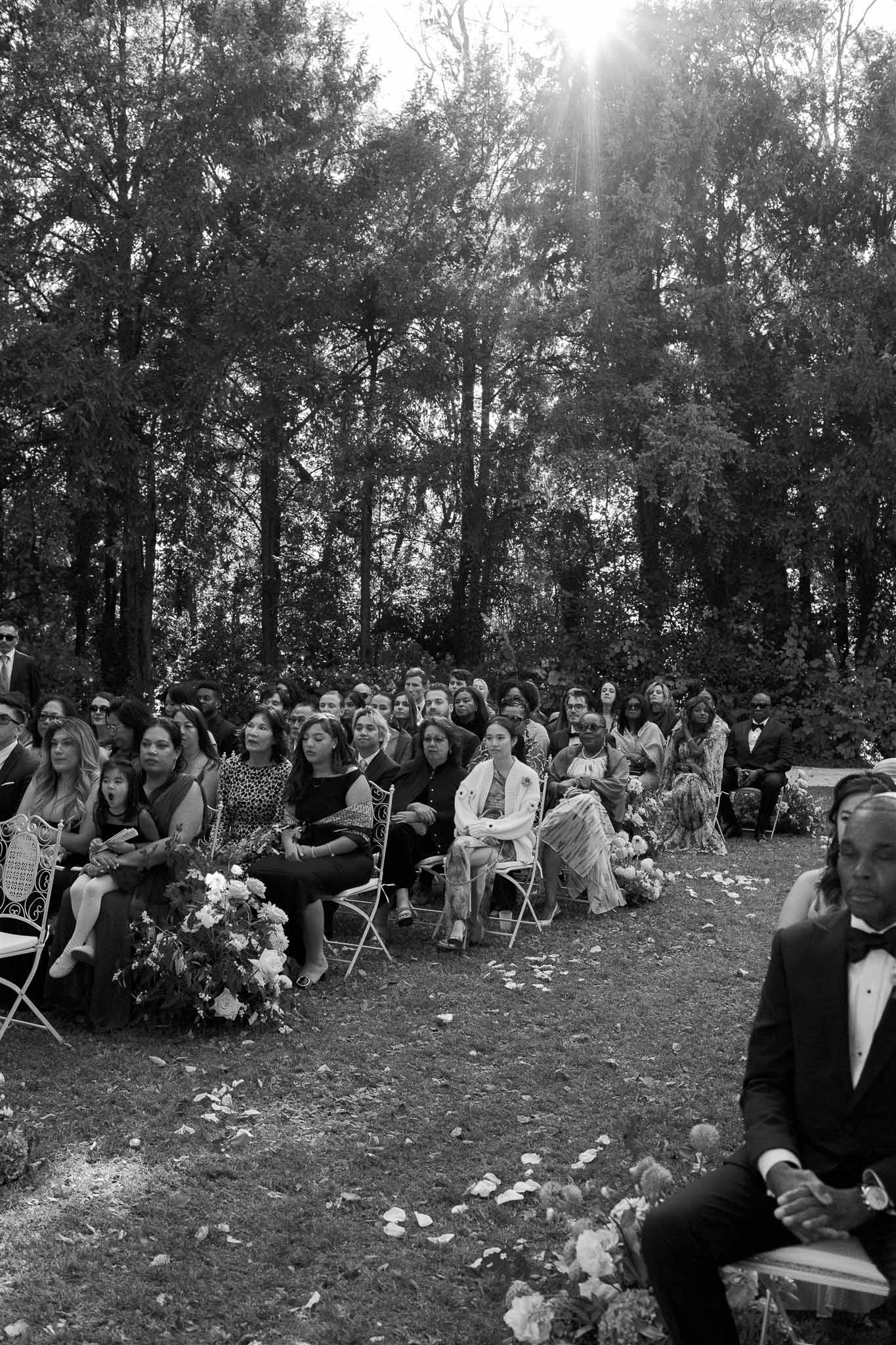 Wedding ceremony with guests seated in forest setting with white floral arrangements