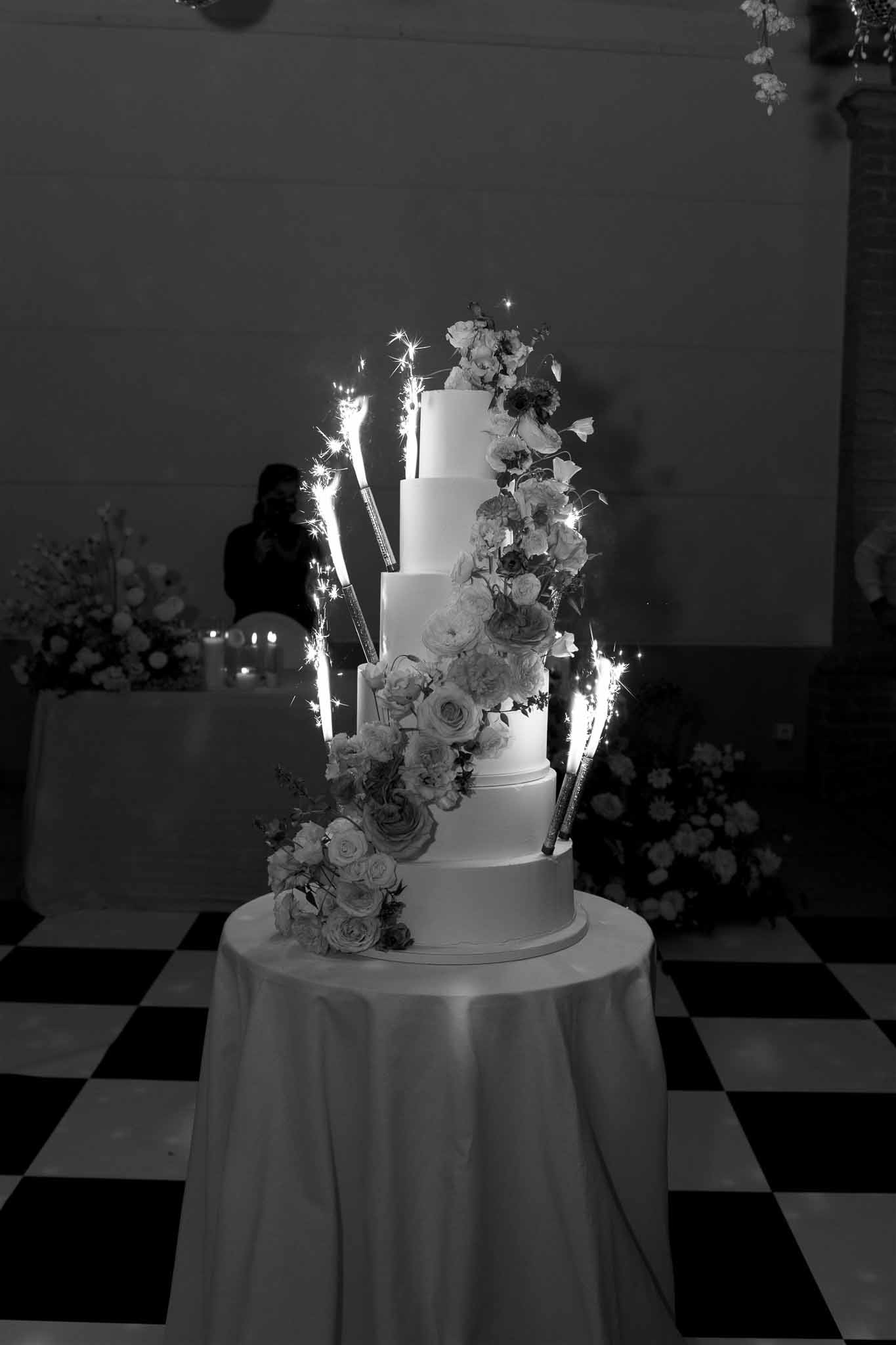 Four-tier wedding cake with sparkler fountains at indoor reception venue