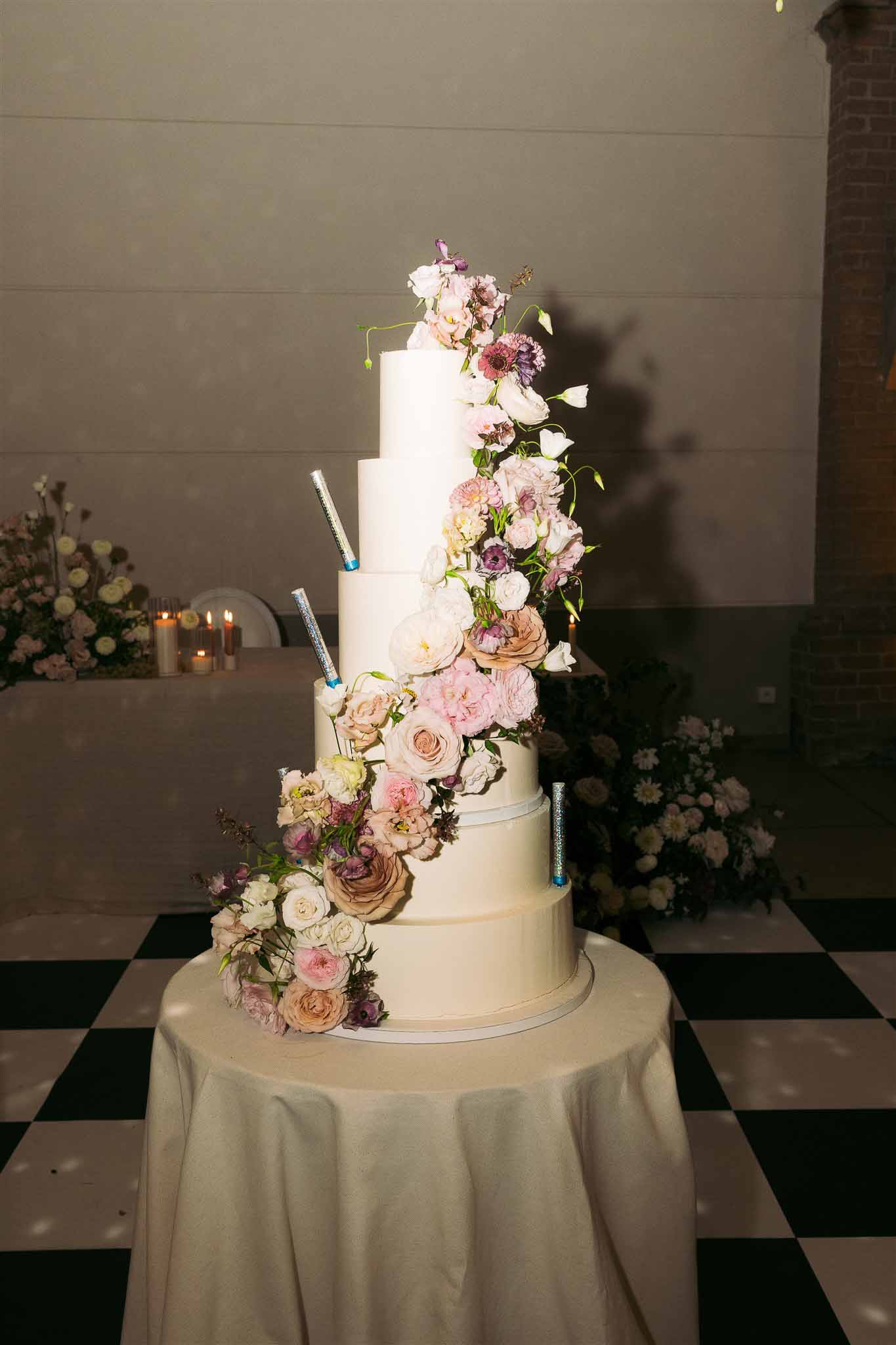 Five-tier ivory wedding cake with cascading dusty rose flowers at indoor reception venue