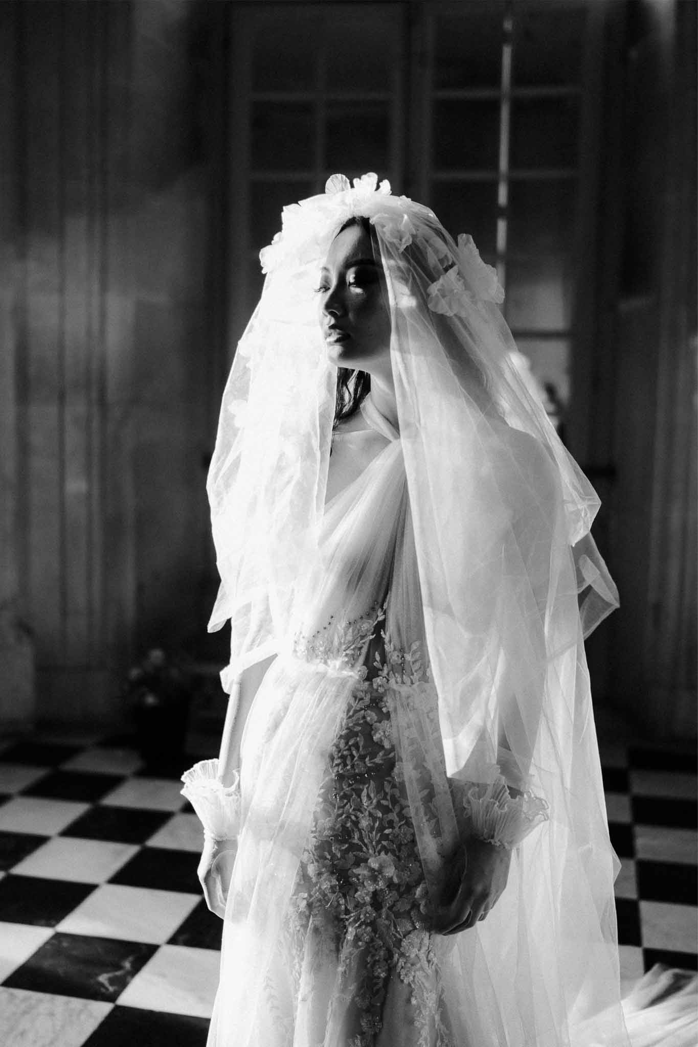 Bride in structured wedding dress with tulle bow veil standing in elegant interior with checkered floor