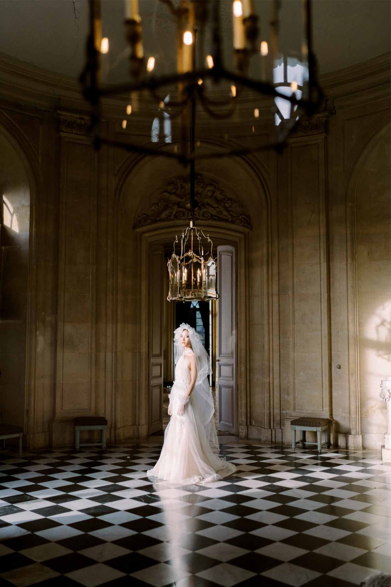 Bride in ivory wedding dress standing in neoclassical hallway with arched details and diamond floor pattern