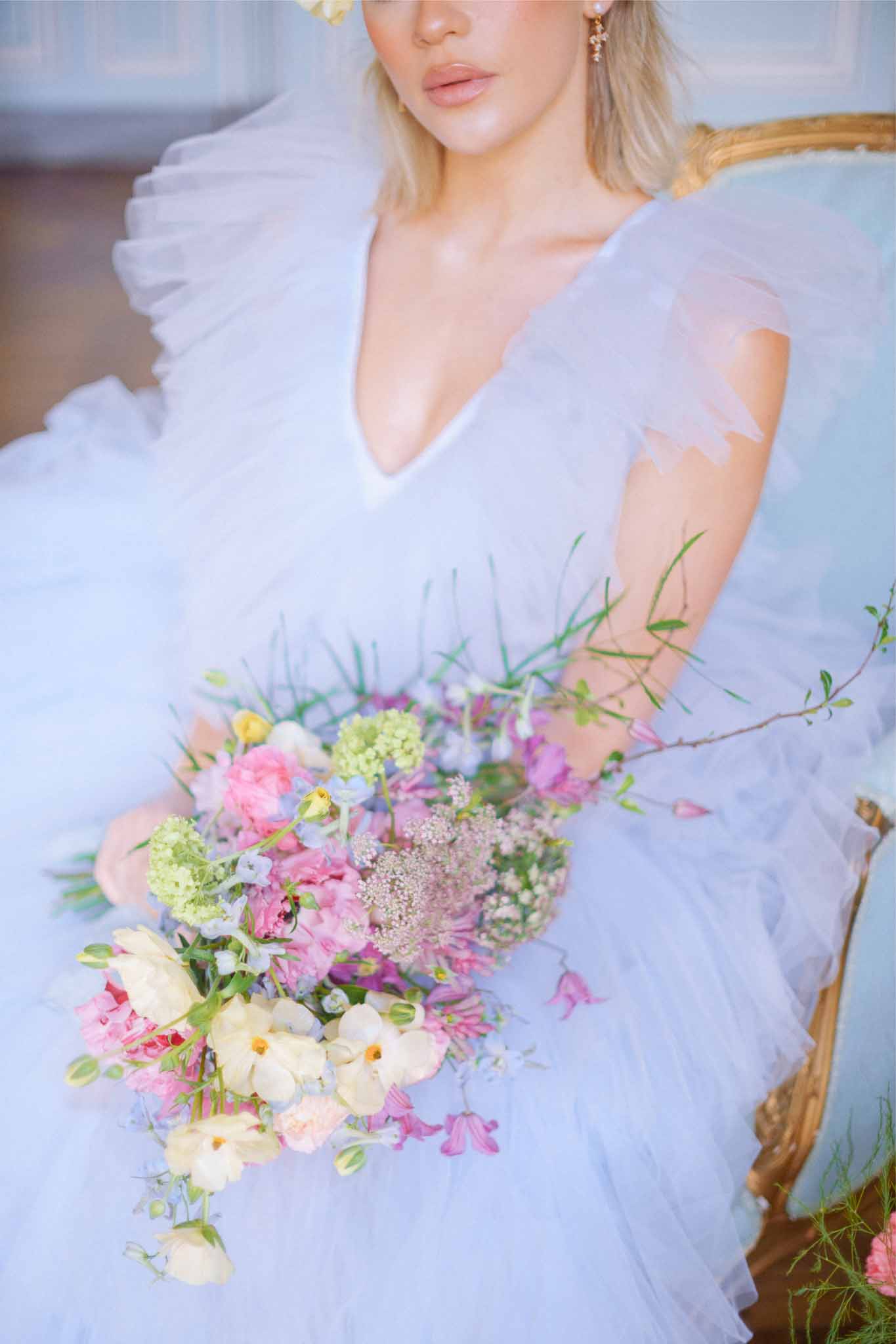 Bride in lavender tulle dress holding garden-style bouquet with peonies and cosmos in romantic portrait