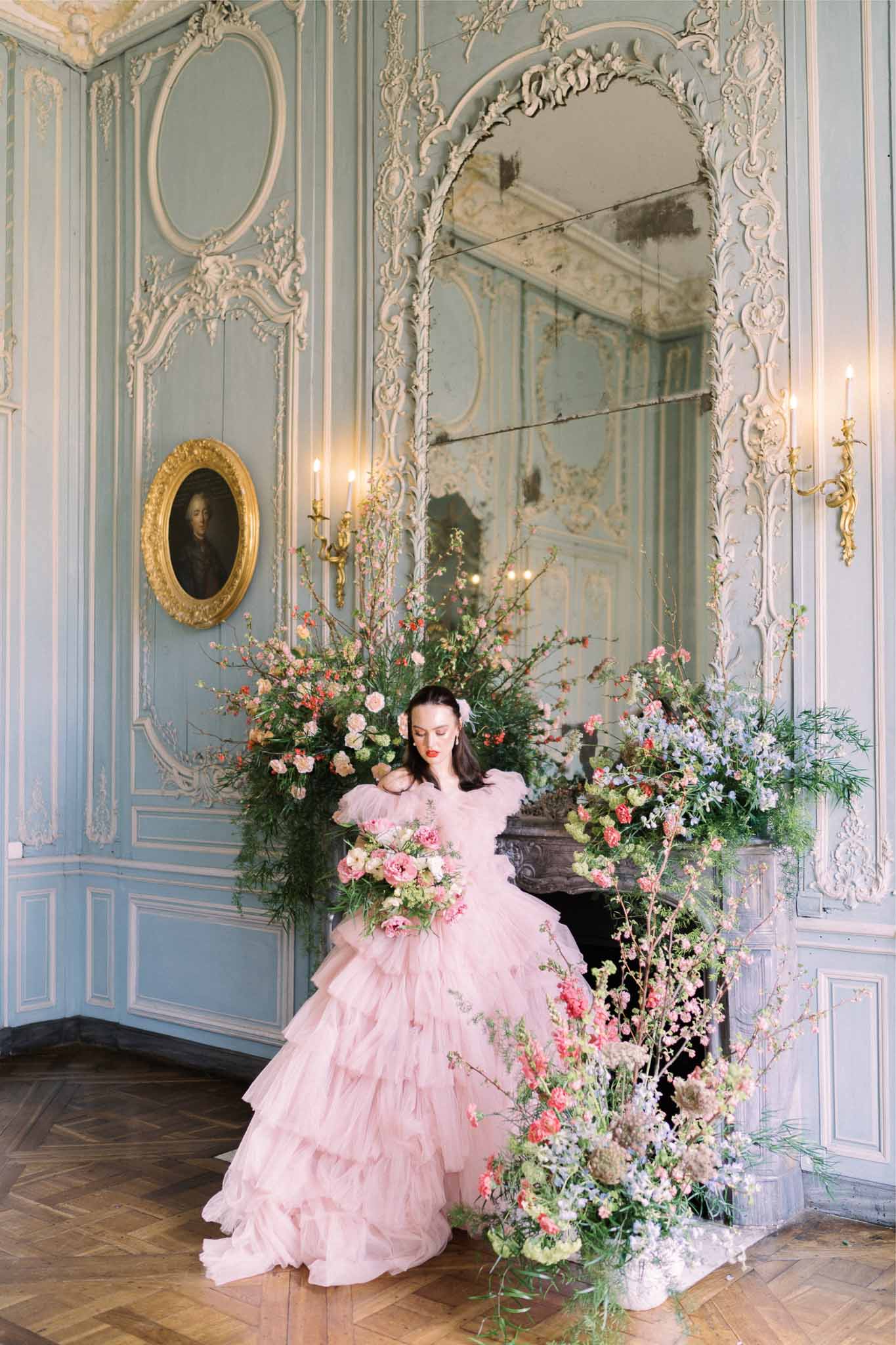 Bride in blush tulle gown with bouquet in ornate neoclassical interior with floral arrangements