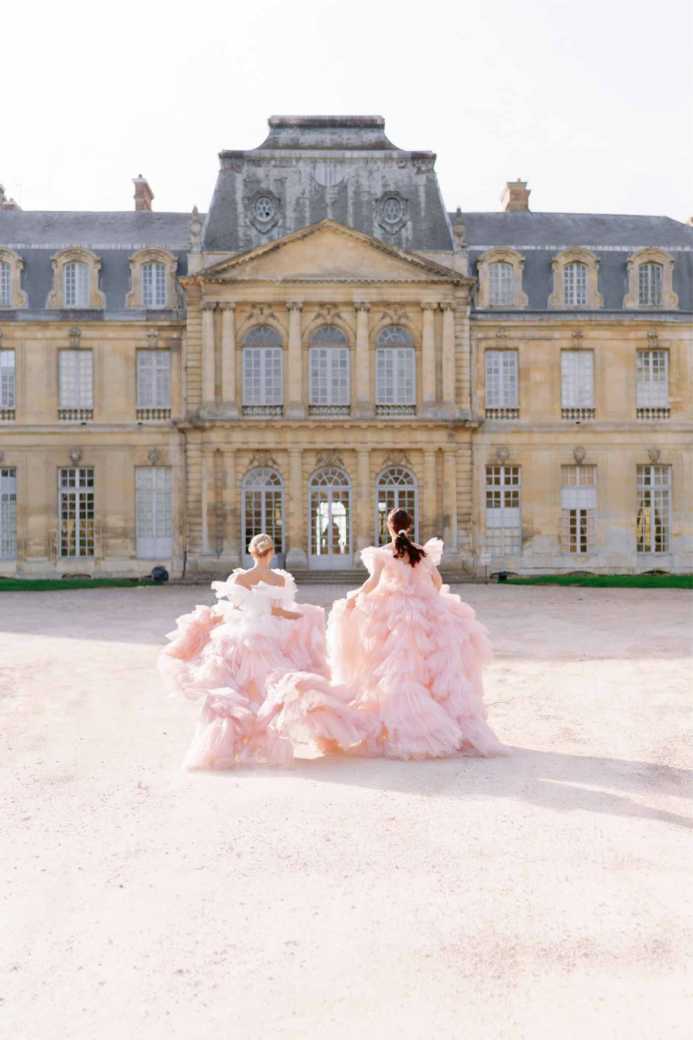 Two bridesmaids in blush pink gowns pose in courtyard of French Baroque château