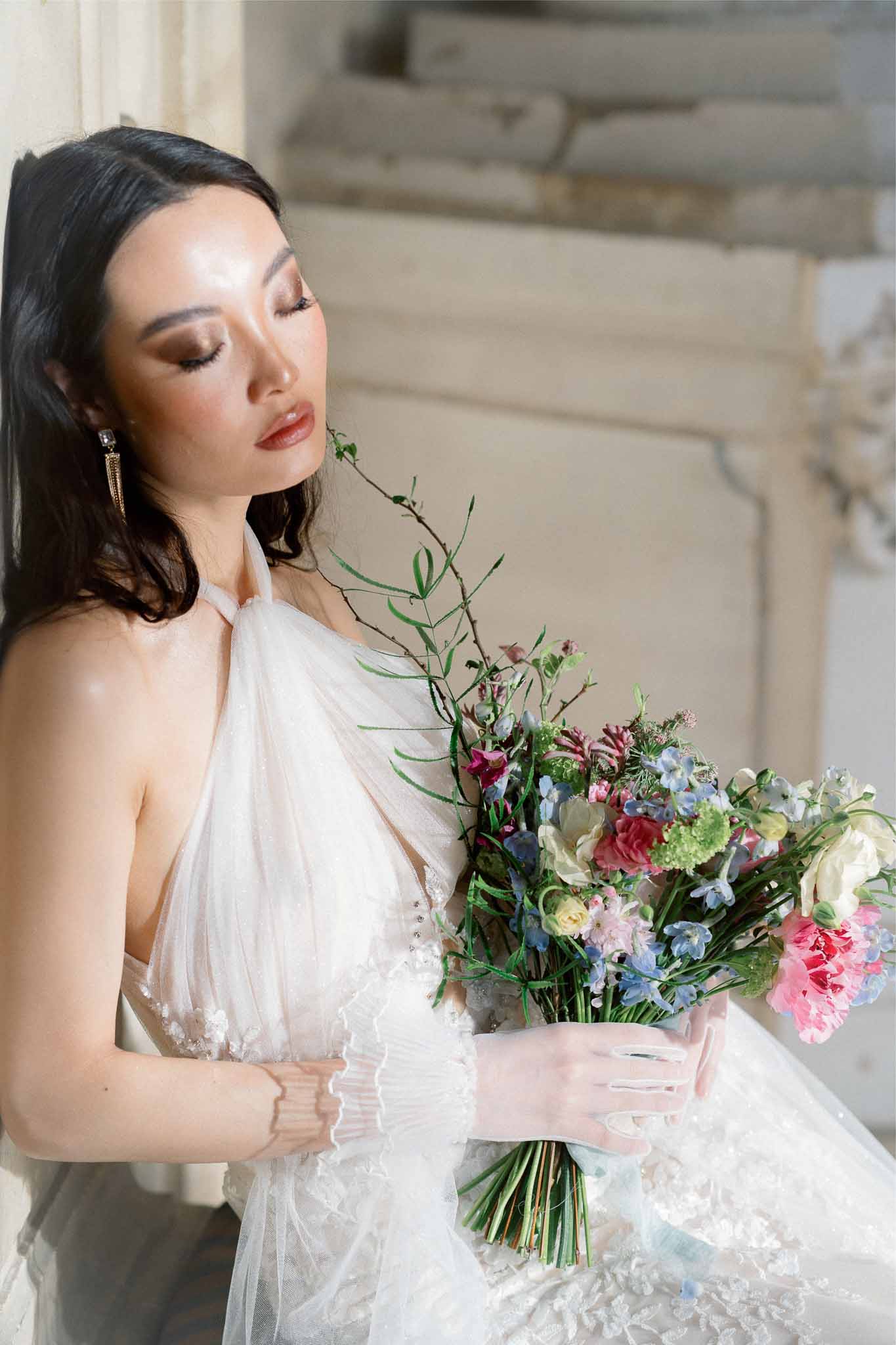 Bride holding garden-style bouquet in ivory halter wedding dress indoors