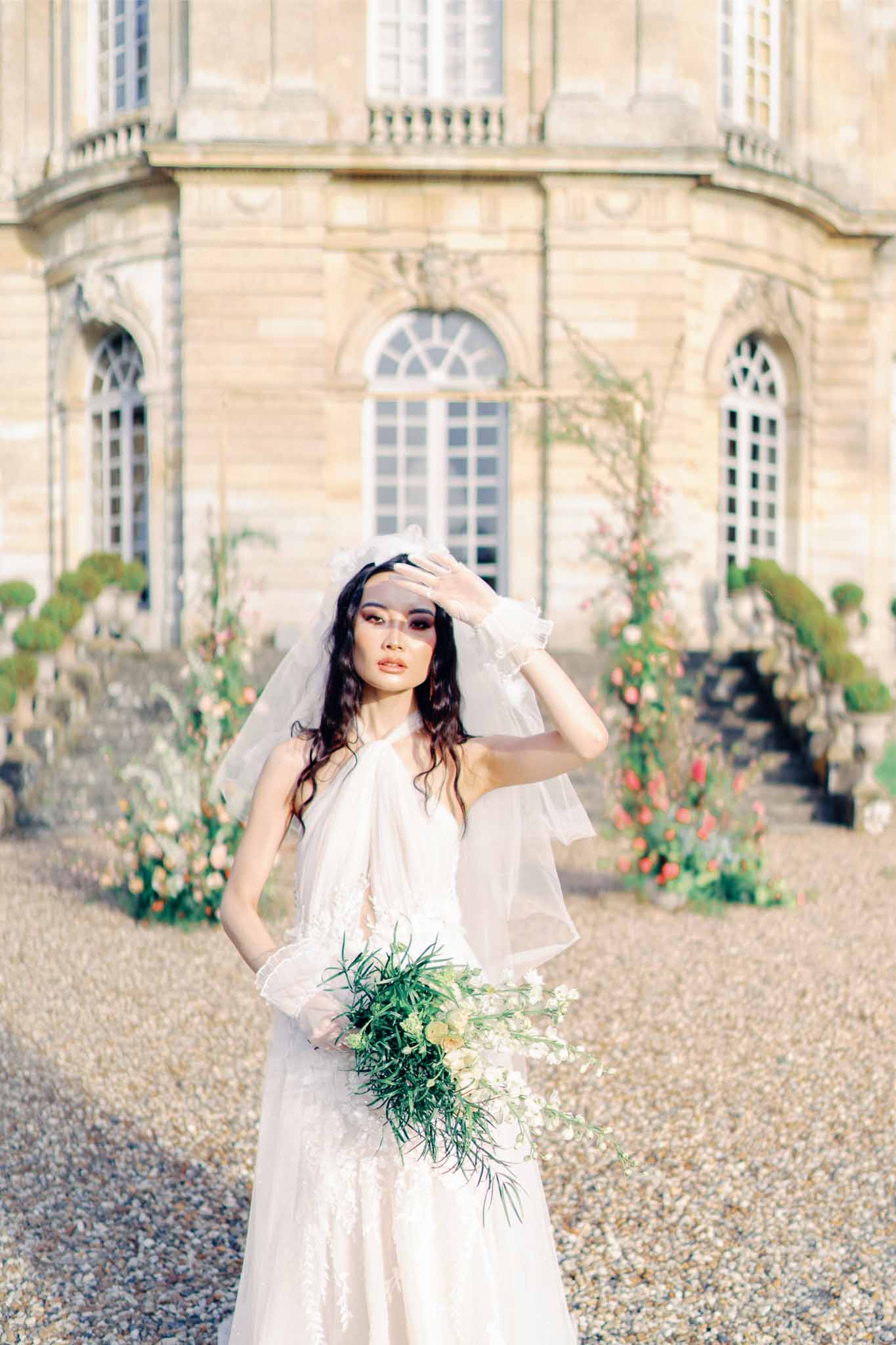 Bride in ivory dress holding peach bouquet at classical stone château courtyard