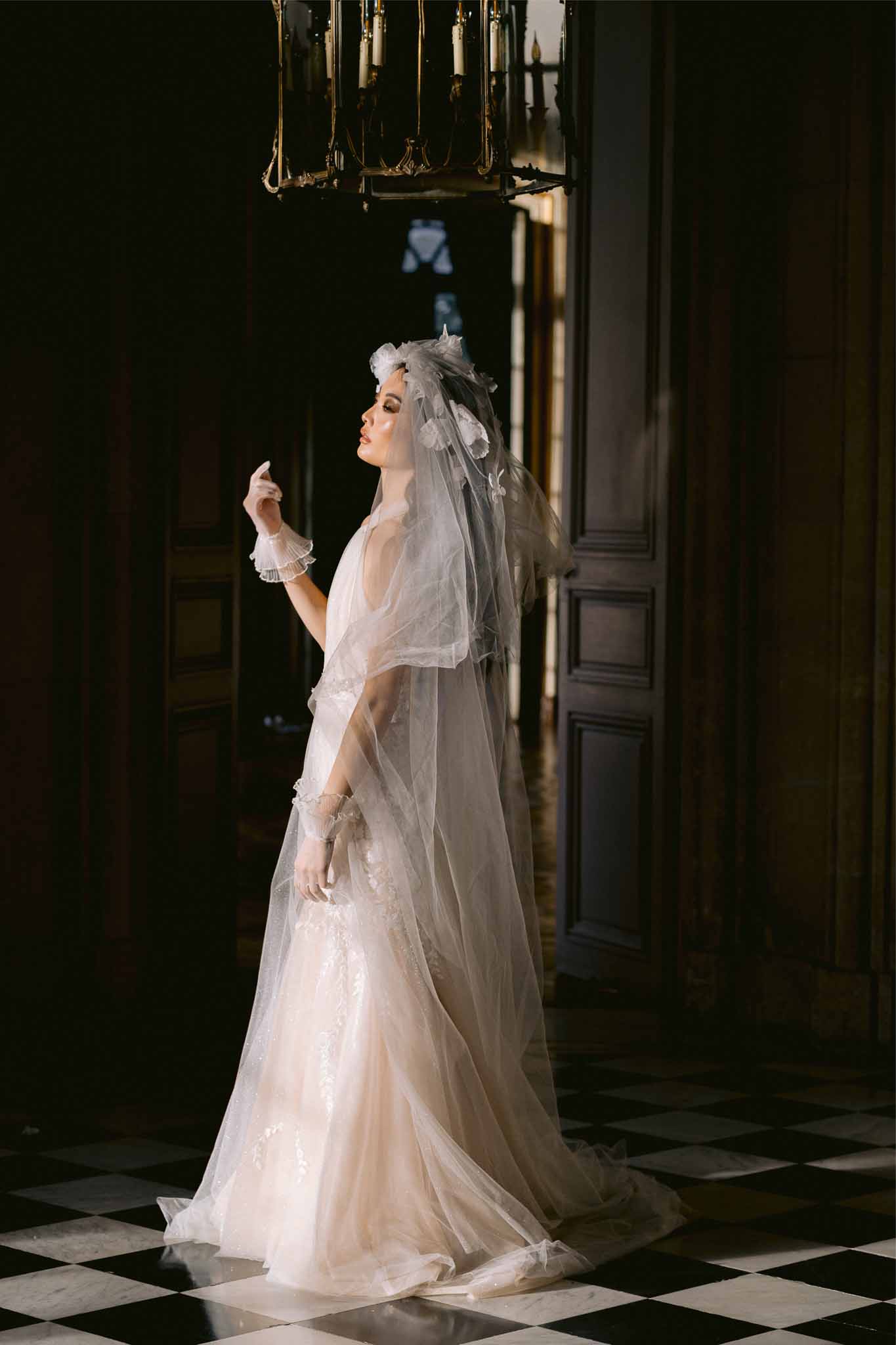 Bride in ivory gown with veil standing in classical hallway with checkered floors