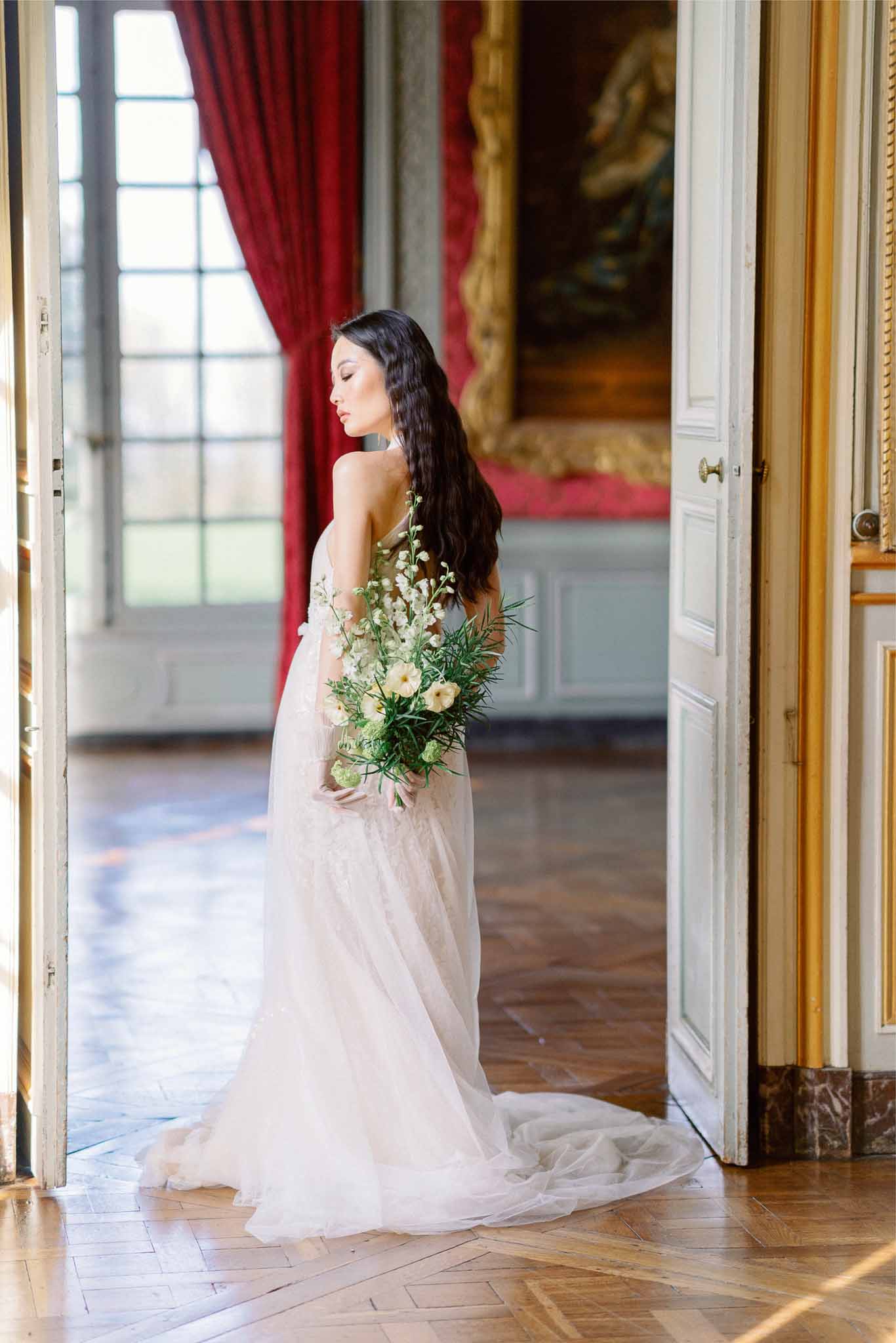Bride in ivory tulle gown holding bouquet in classical ballroom doorway