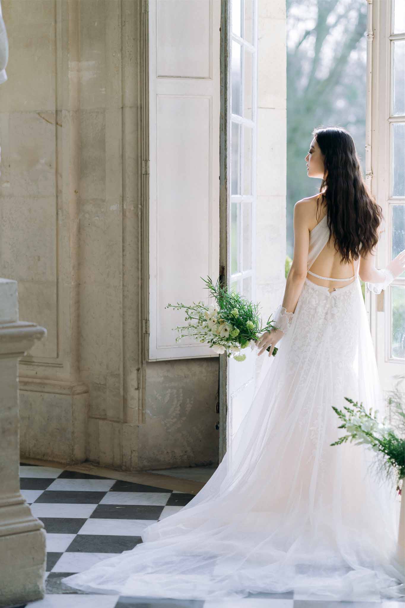 Bride in ivory crop top and tulle skirt holding white bouquet in classical indoor hallway with diamond tile floor