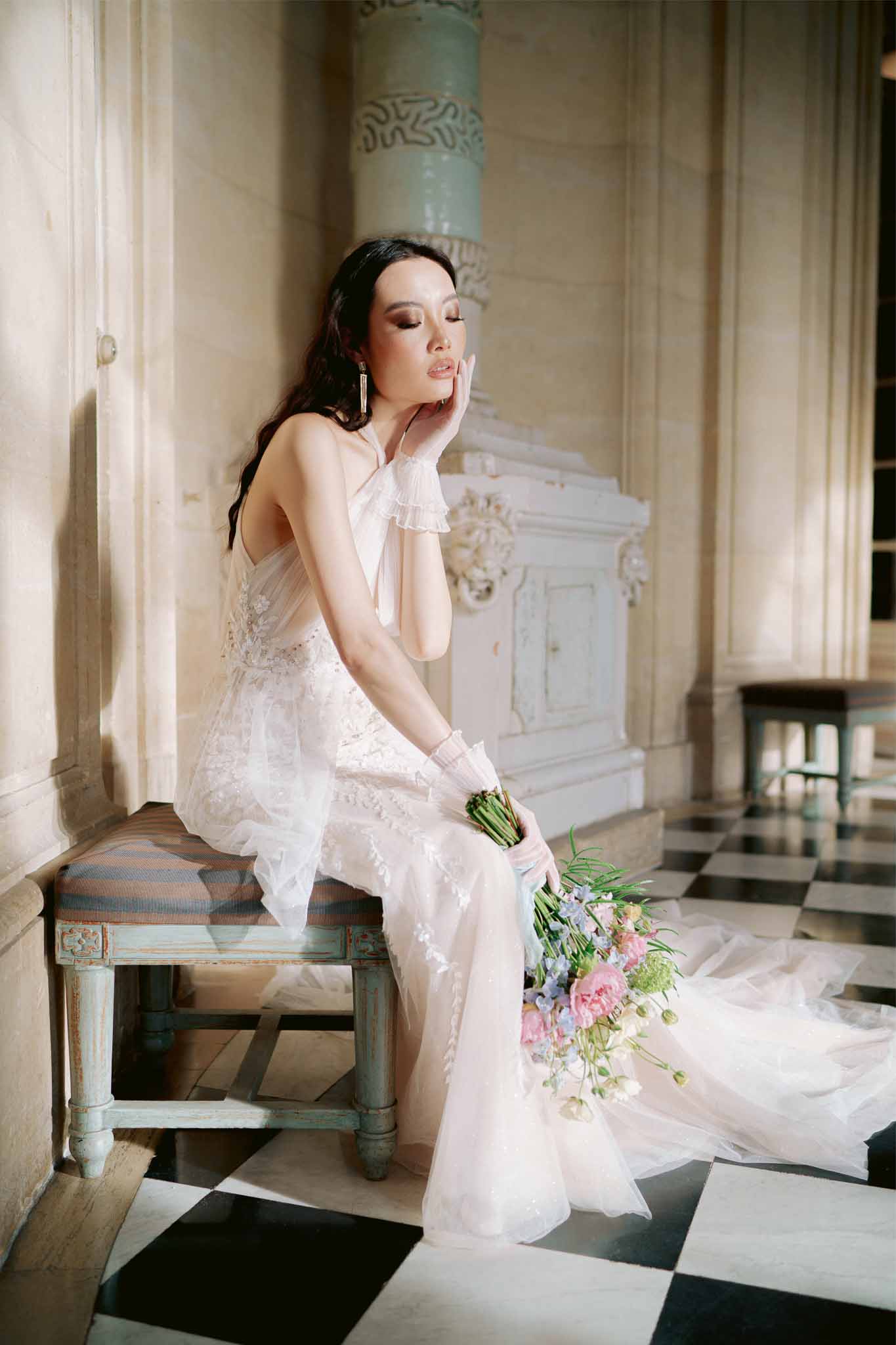 Bride in ivory lace wedding dress with bouquet sitting in classical interior with columns and molding