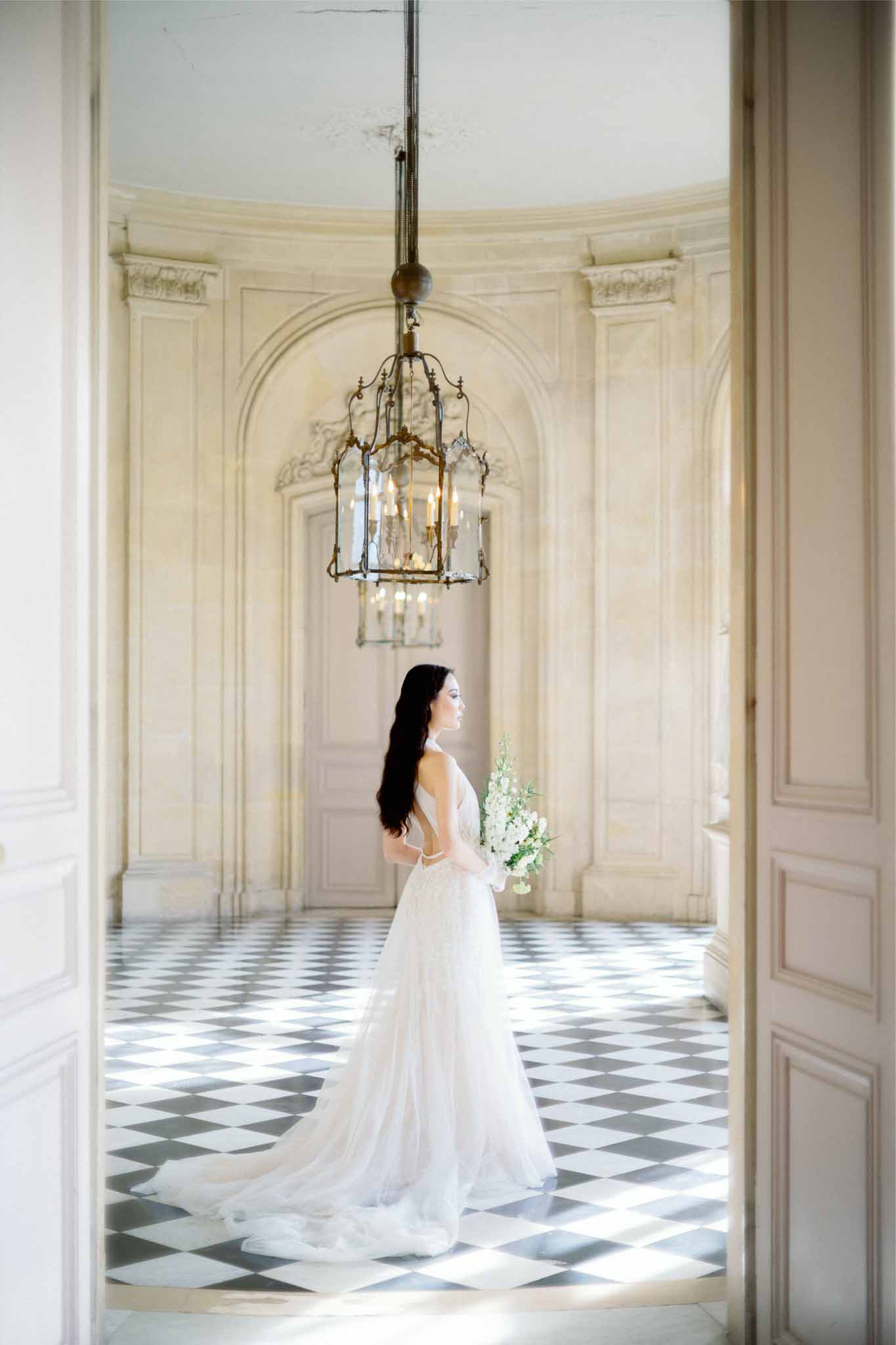 Bride in ivory gown standing in neoclassical interior with marble floors and arched doorways