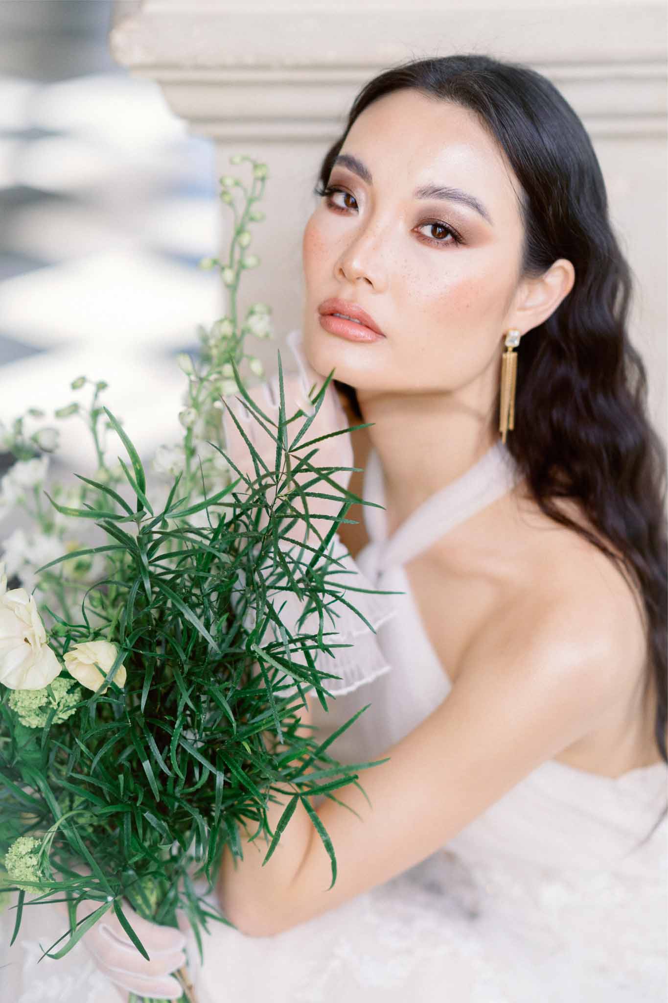 Bride holding minimalist bouquet with cream roses and asparagus fern in indoor portrait