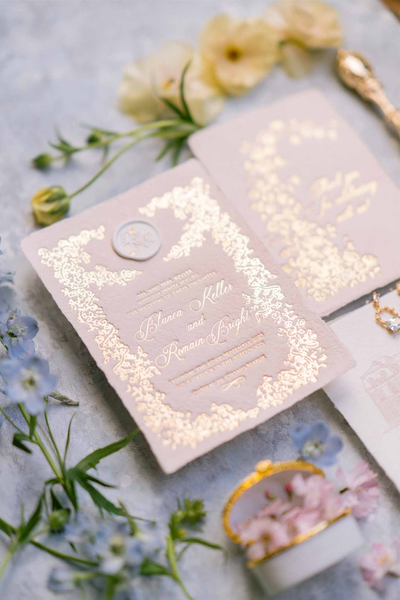 Wedding invitation flat lay with rings and ranunculus flowers on marble surface