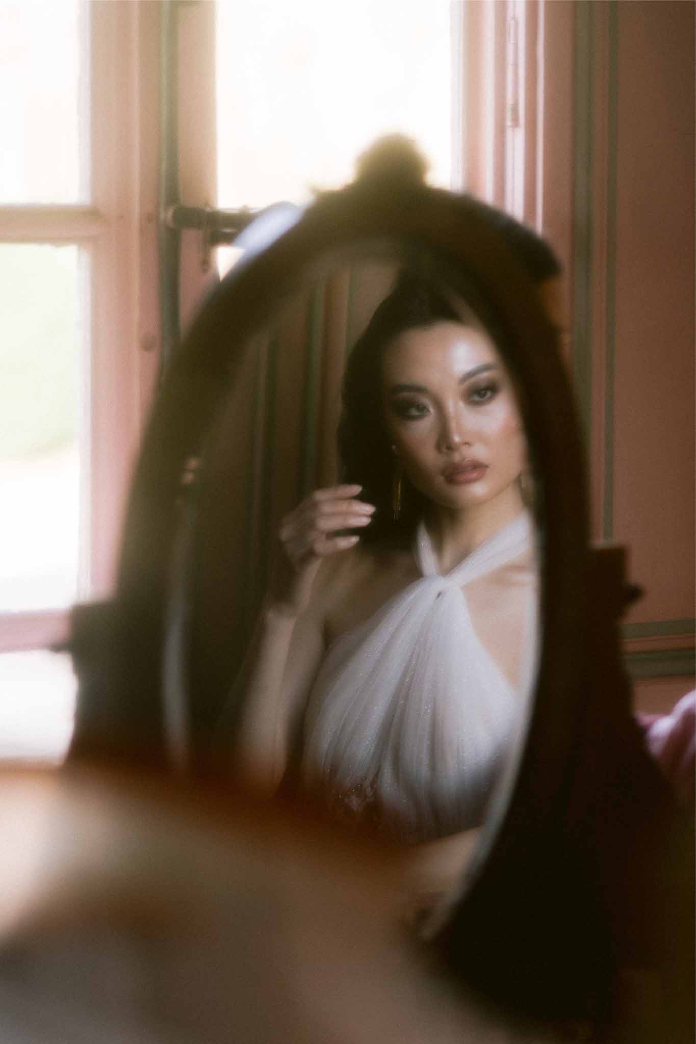 Bride in ivory dress being assisted with veil during getting ready moment indoors near windows