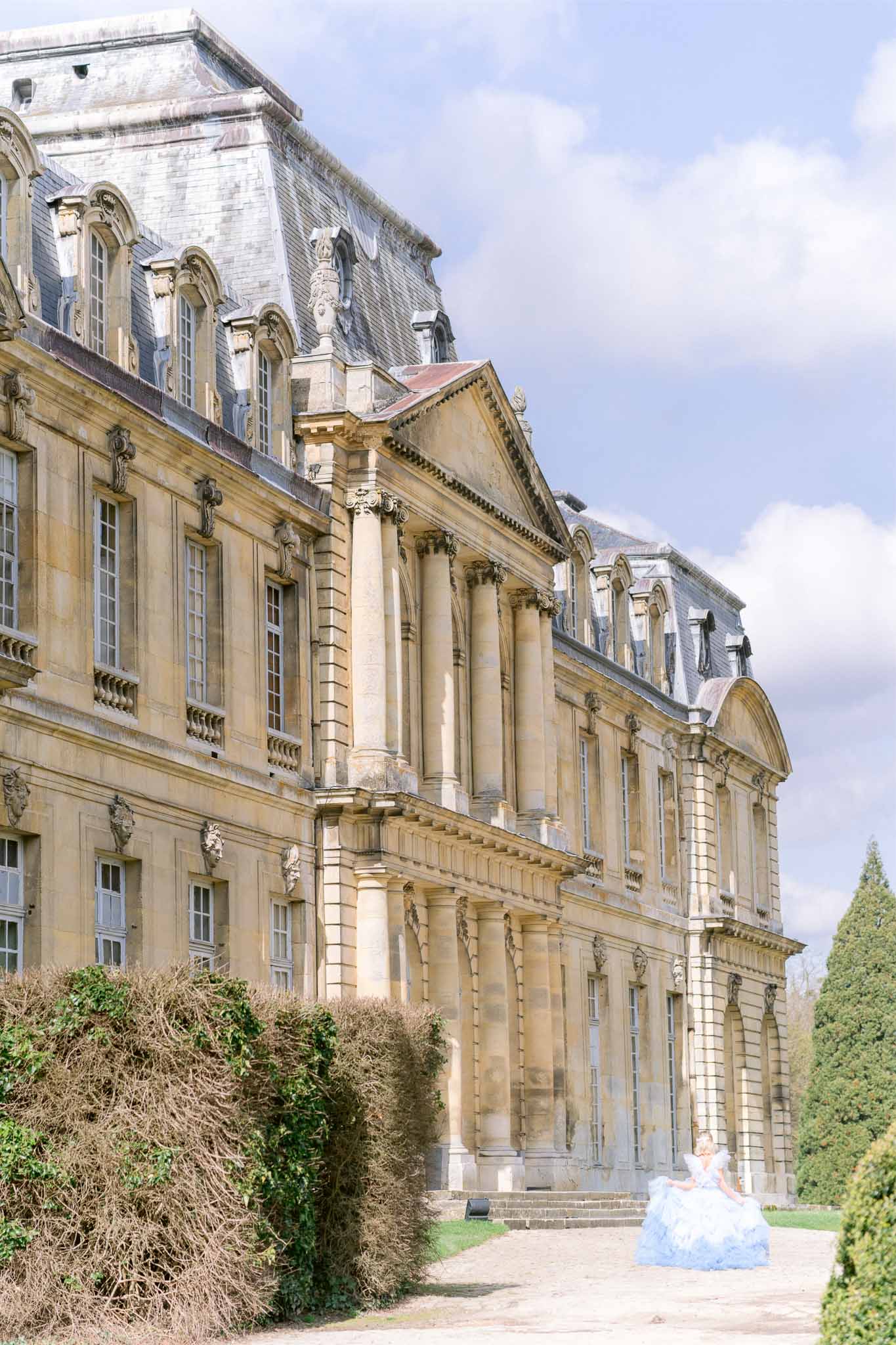 Bride in white ballgown standing before grand neoclassical château with Corinthian columns