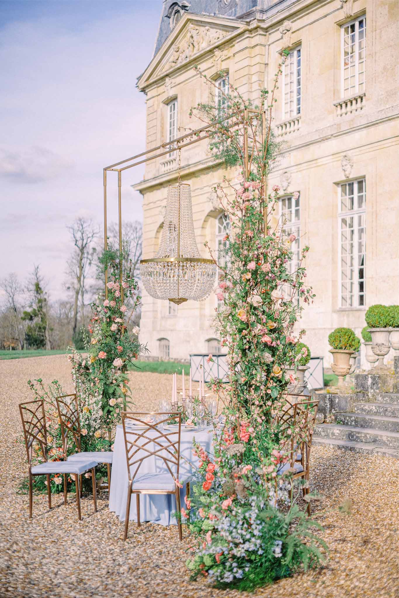 Intimate outdoor reception setup with floral arch in château courtyard