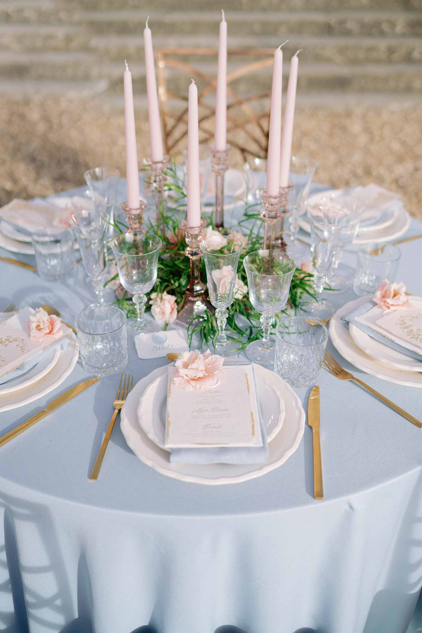 Formal reception table setting with pale blue linens, gold flatware, and pink floral centerpiece