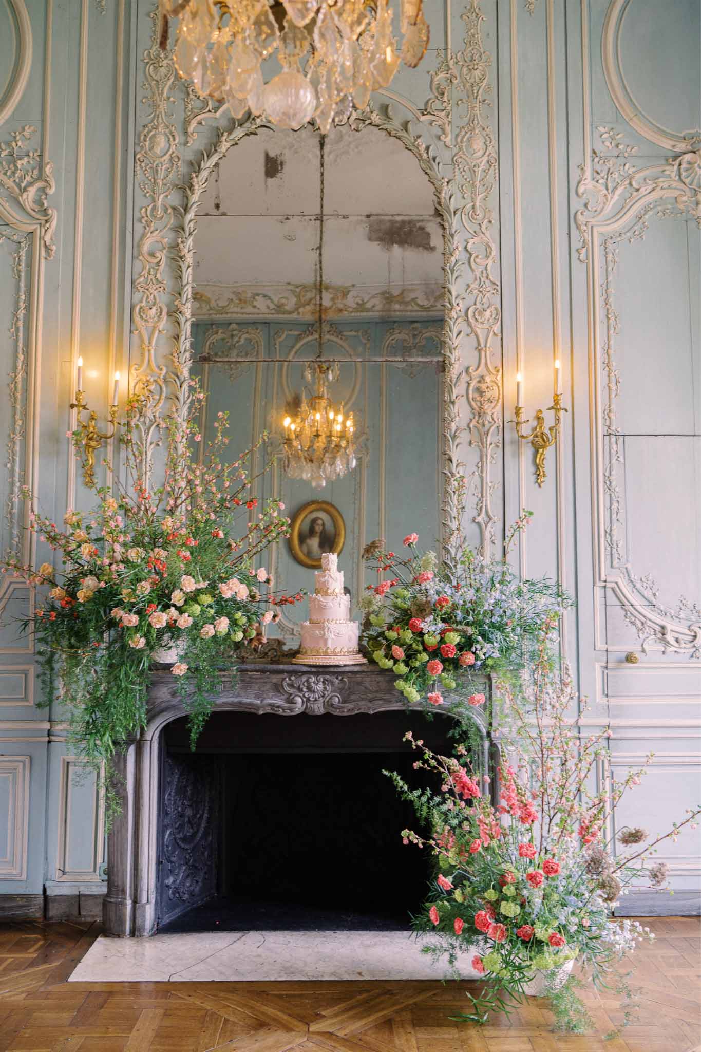 Wedding cake and floral display on marble mantelpiece in ornate French salon with gilded details