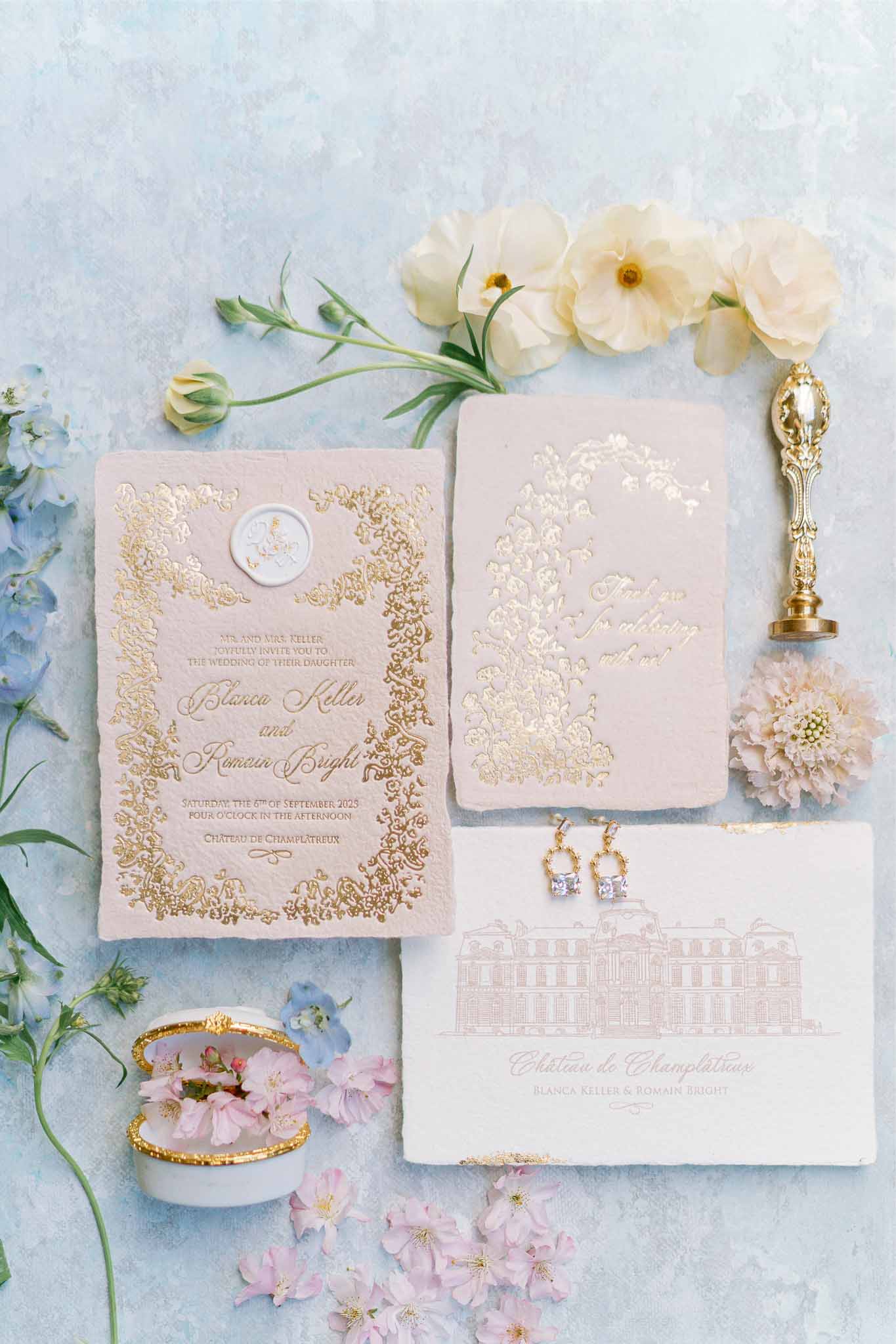 Wedding invitation suite and accessories arranged with flowers on textured background