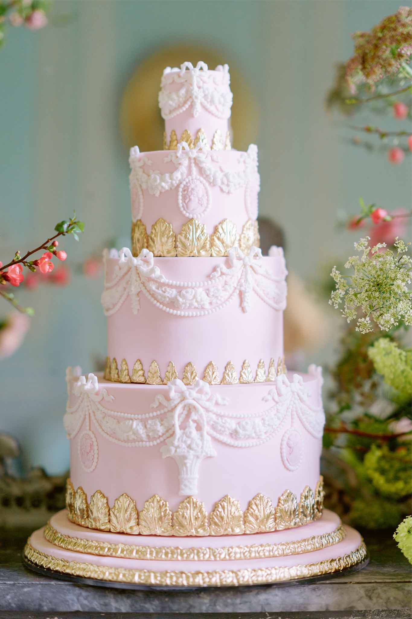 Five-tiered wedding cake with pink and white fondant, gold details, and fresh coral flowers