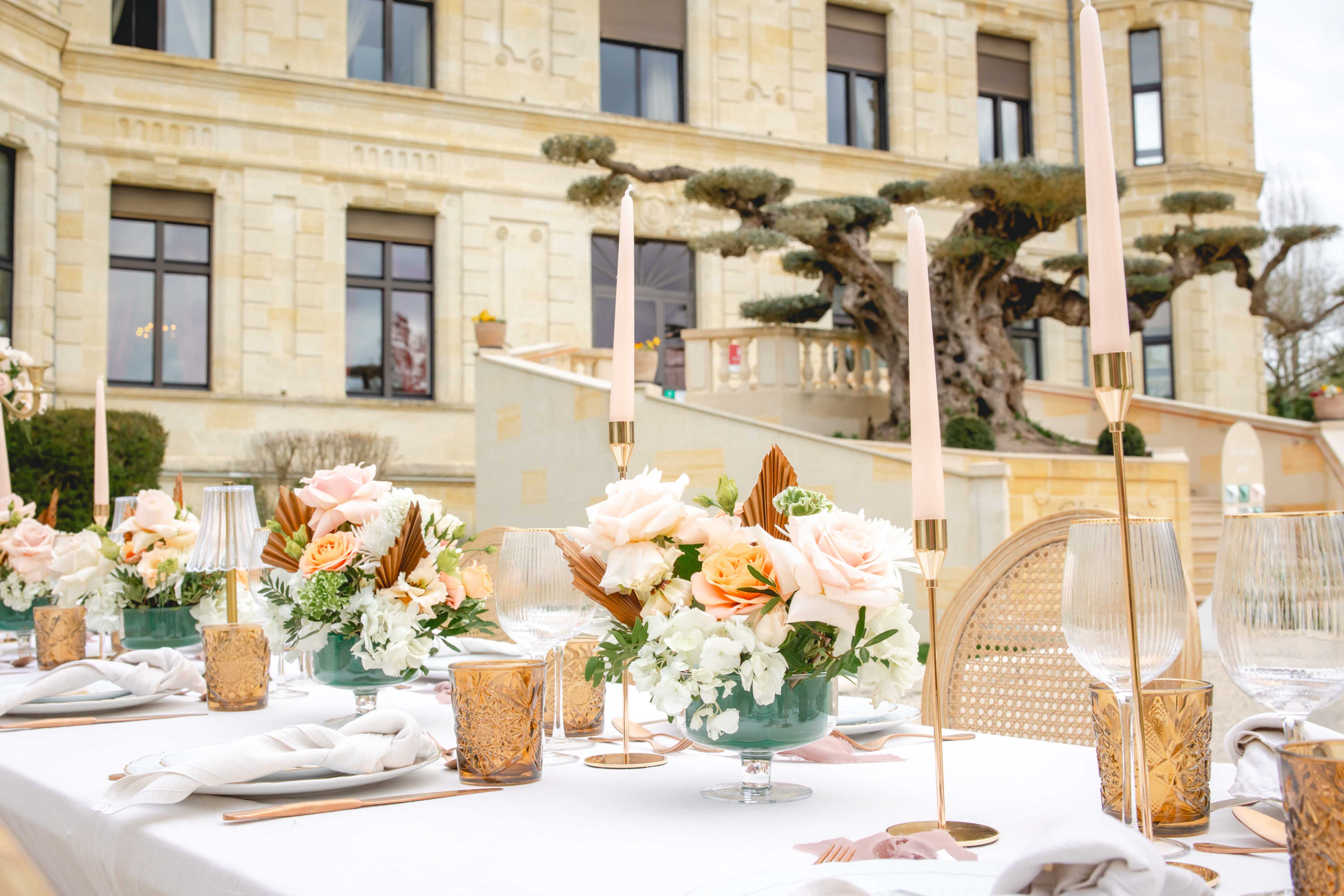 Reception table with blush roses in teal bowls, gold candleholders, and dried palm leaves at chateau