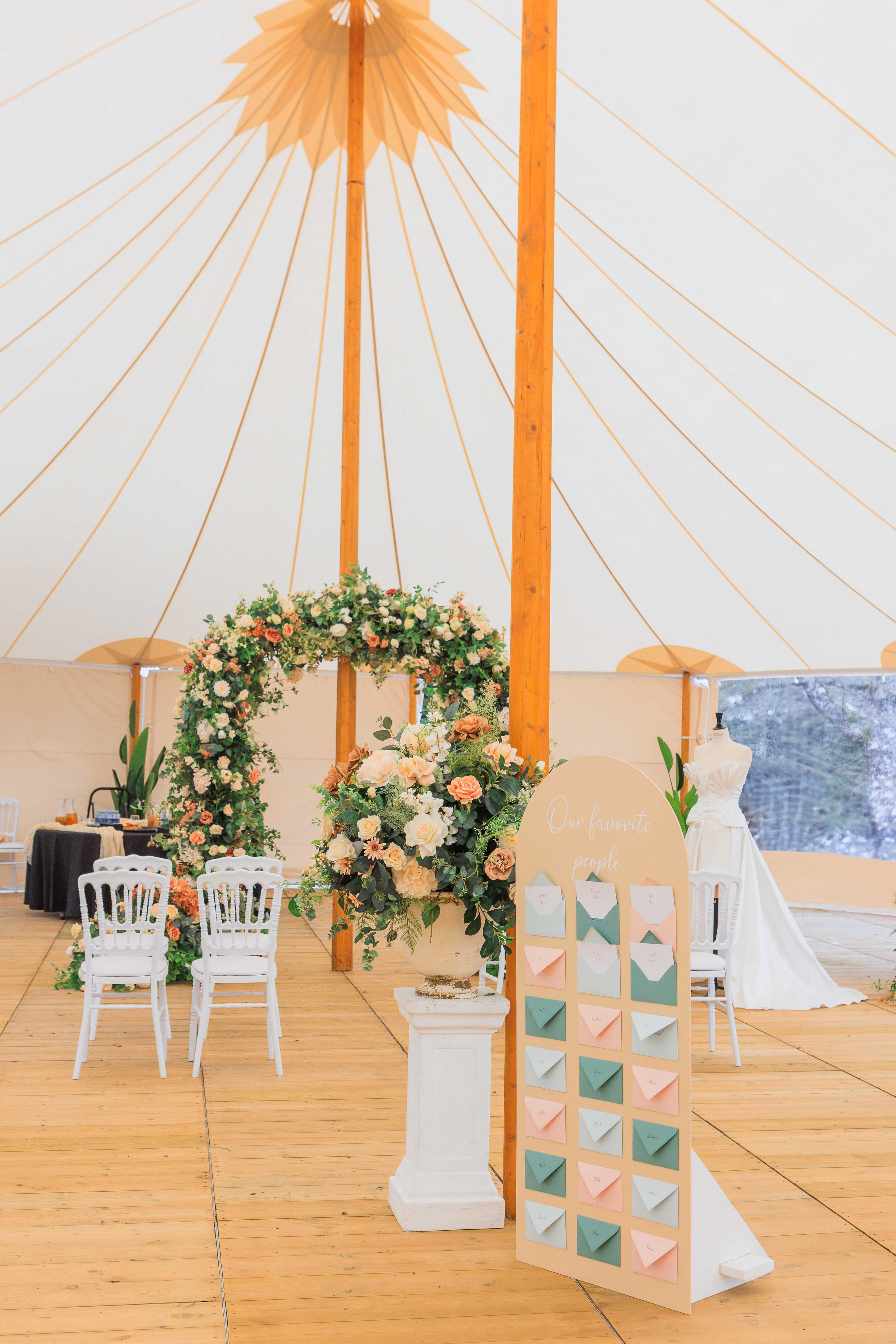 Spire tent interior with circular floral arch in peach and terracotta tones, seating chart, and displayed gown