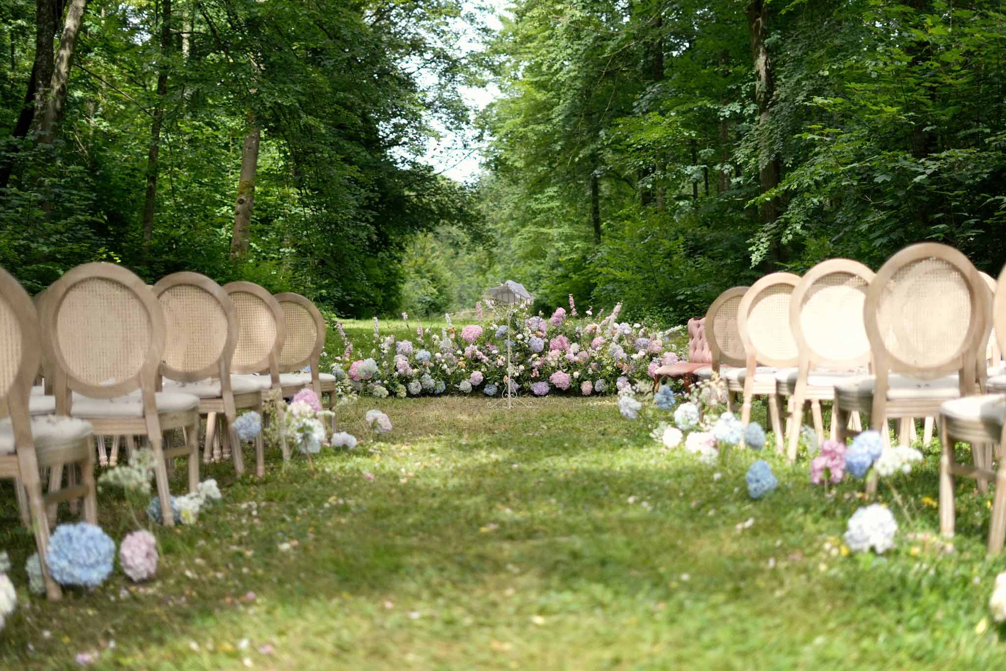 Outdoor ceremony setup with wooden chairs and hydrangea arrangements in wooded garden setting