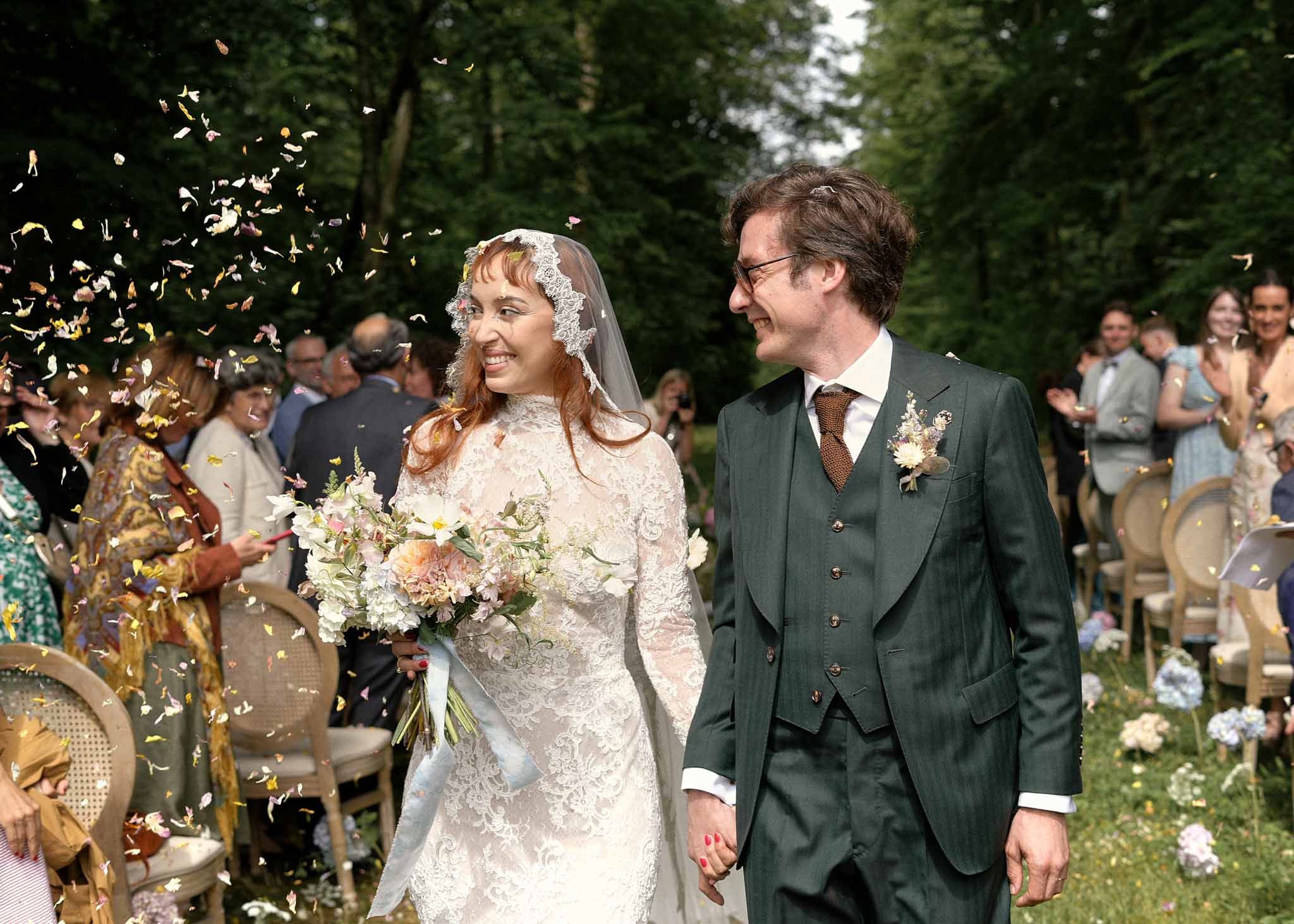 Bride and groom walking down aisle after outdoor garden ceremony with confetti and floral decor