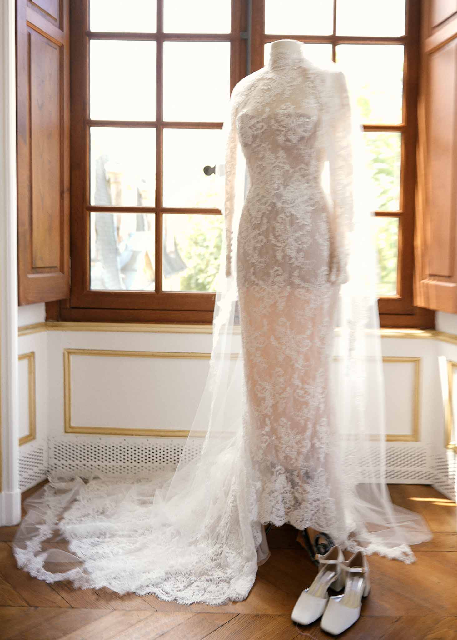 Ivory lace wedding dress with cathedral veil displayed on mannequin in elegant interior room