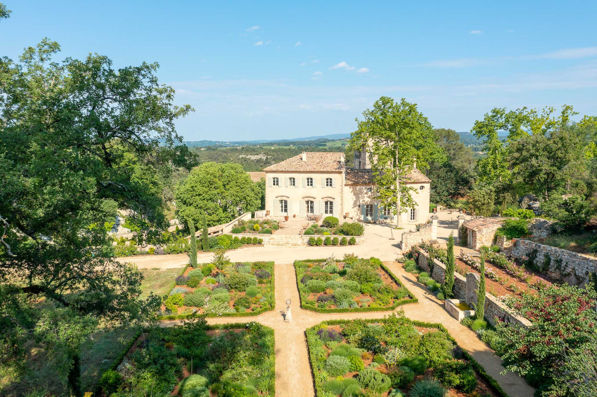 Aerial view of Provencal stone manor with terracotta roof, parterre garden, and valley landscape beyond