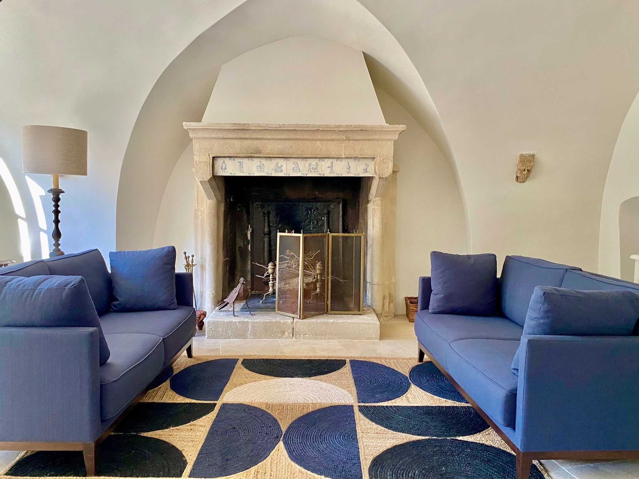 Chateau lounge with stone fireplace, blue-and-white tiled mantel, navy sofas, and vaulted stone arches