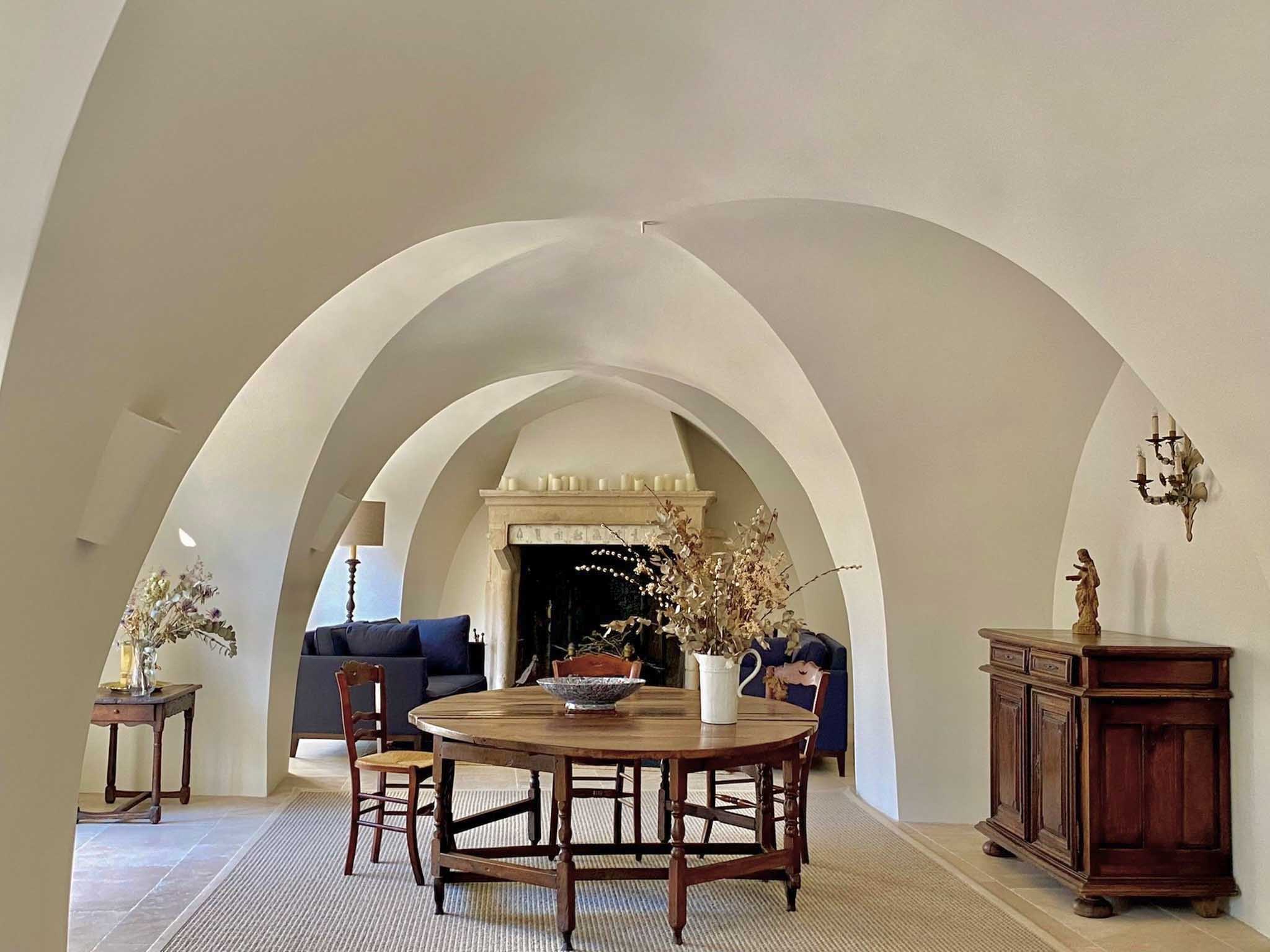 Barrel-vaulted white plastered interior with walnut table rush chairs fireplace and dried flowers