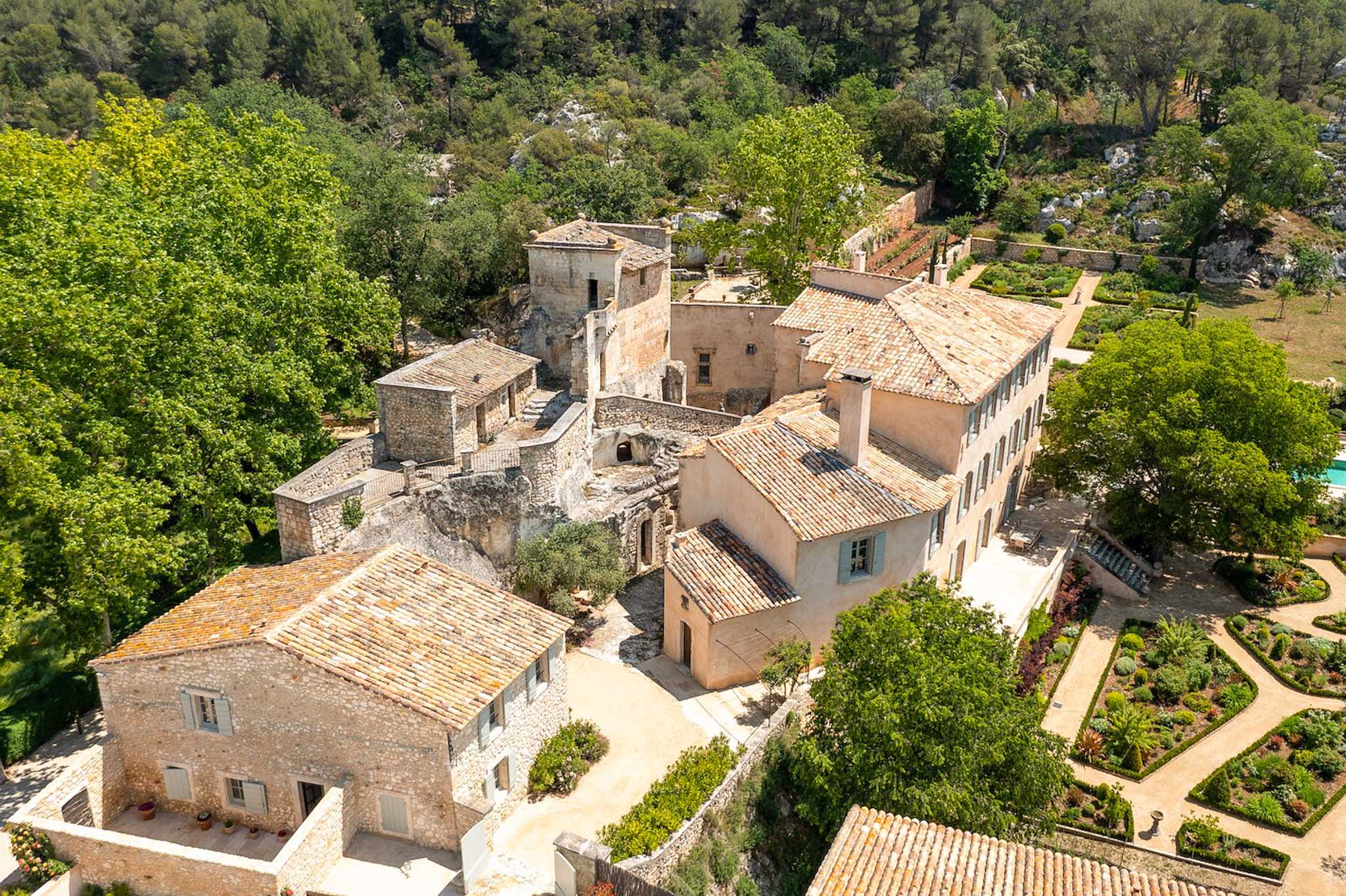 Aerial drone view of a Provencal stone property with terracotta roofs, parterre gardens, and swimming pool