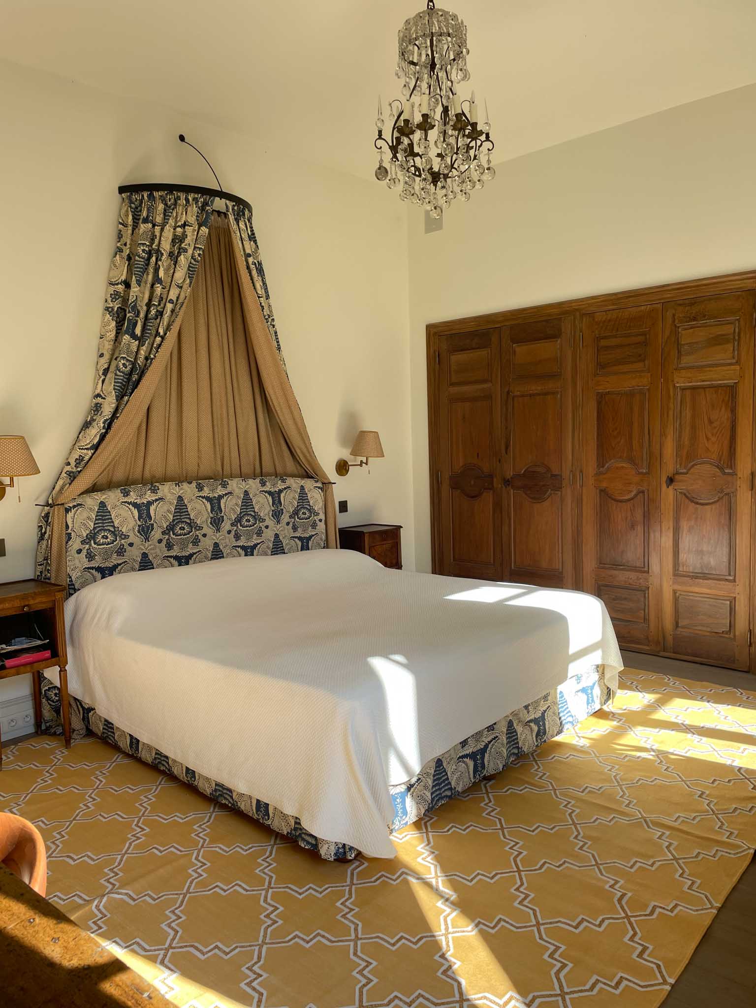 Chateau bedroom with blue paisley headboard, gold canopy draping, antique armoires, and crystal chandelier
