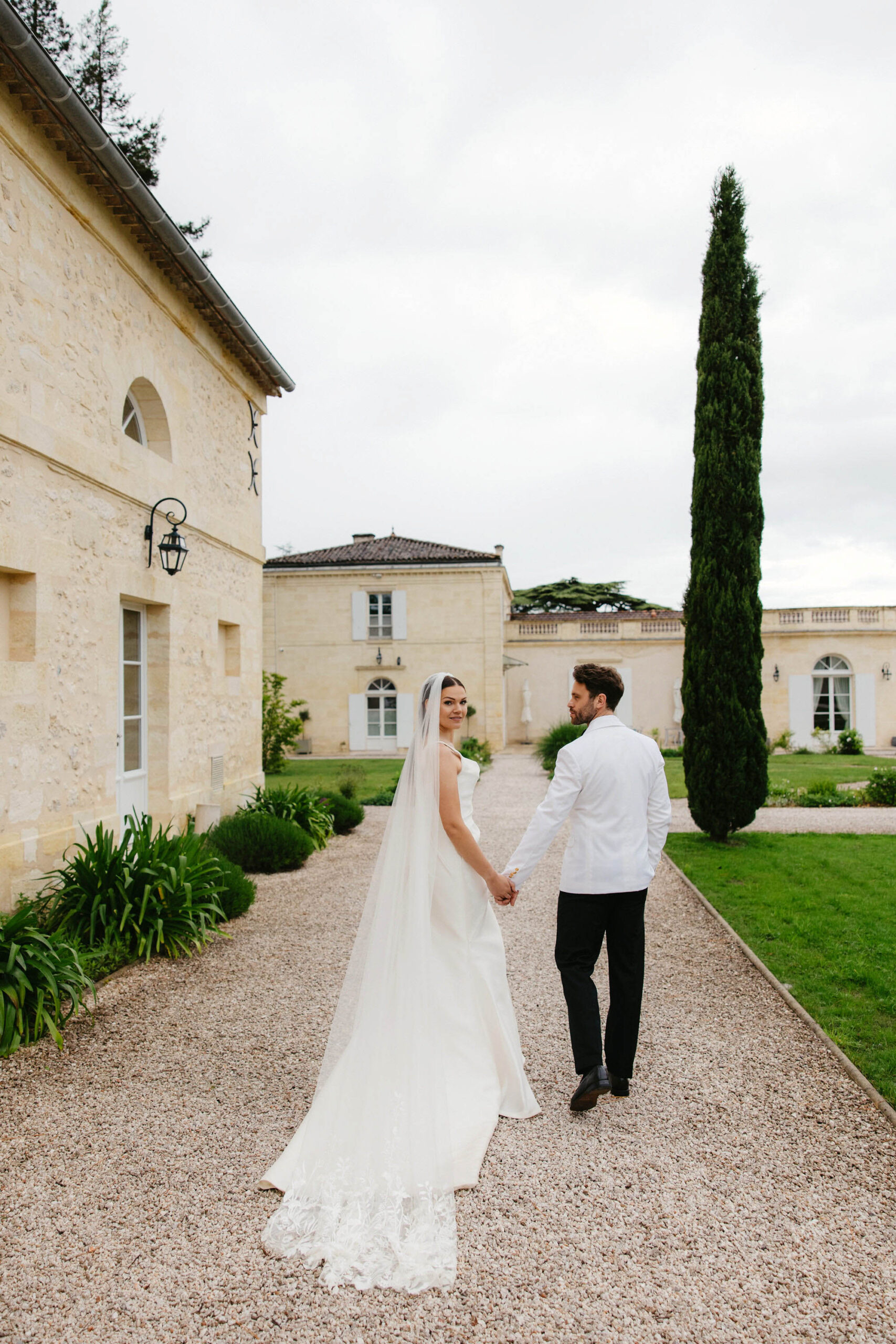 Bride and groom holding hands on gravel courtyard of French limestone chateau