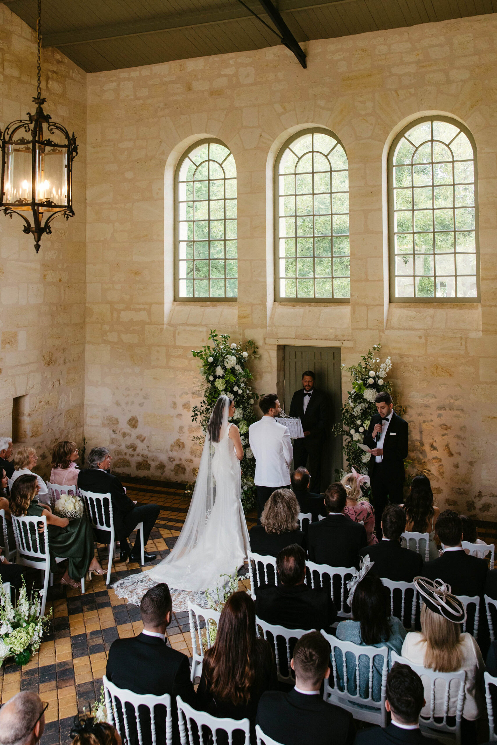 Indoor stone chapel ceremony with white floral altar arrangements and 40 guests on Chiavari chairs